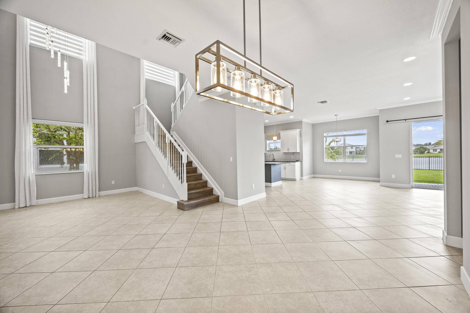 16007 Whippoorwill Circle, Westlake, Westlake, FL 33470 Expansive open-concept living area featuring large format tile flooring, a prominent staircase with wood-finish treads, and a modern linear chandelier