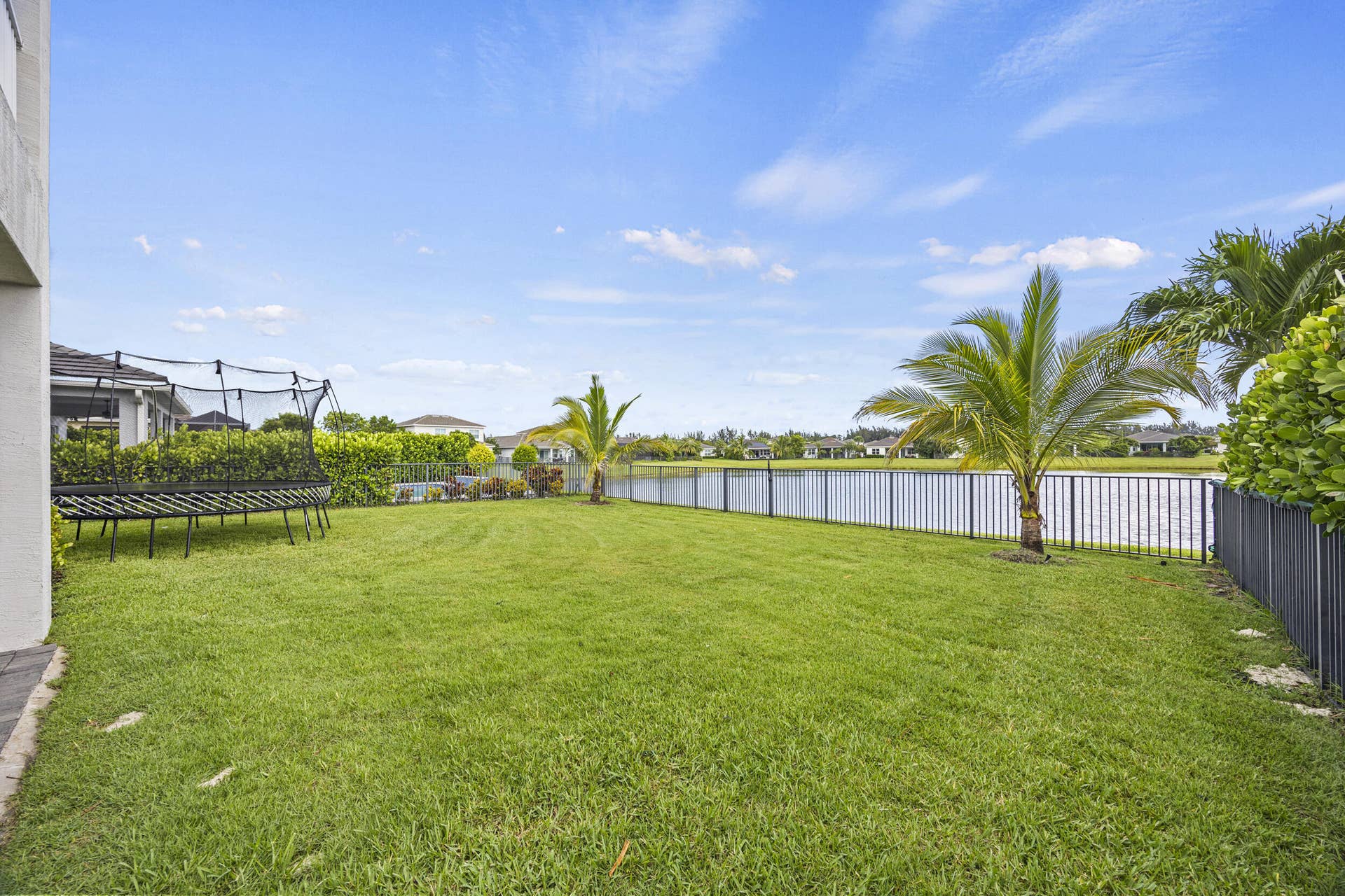 16007 Whippoorwill Circle, Westlake, Westlake, FL 33470 Expansive green lawn with a black metal fence bordering a water feature, featuring mature palm trees and landscaped shrubbery