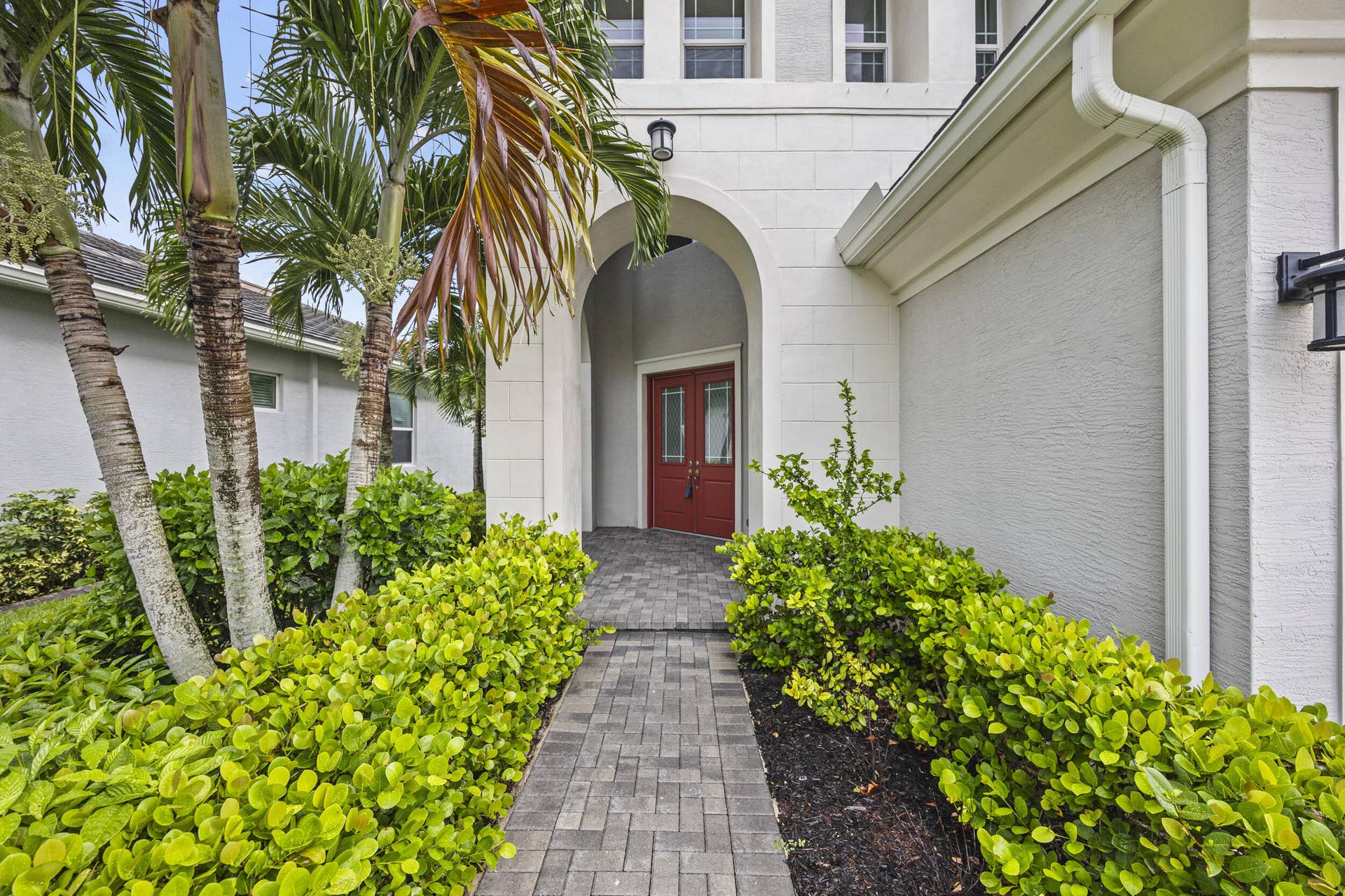 16007 Whippoorwill Circle, Westlake, Westlake, FL 33470 Paver walkway leading to an arched entry with a red double door, surrounded by established landscaping
