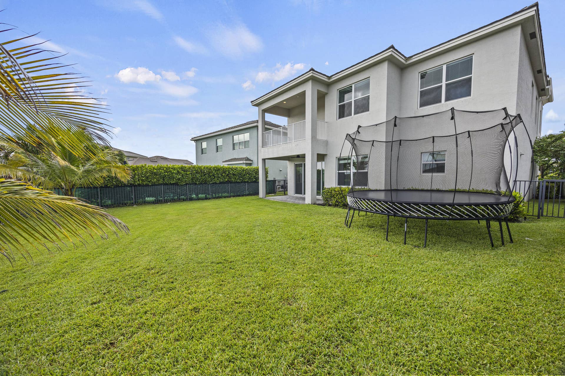 16007 Whippoorwill Circle, Westlake, Westlake, FL 33470 Expansive grassy yard with a two-story stucco exterior, upper-level balcony, and a dark metal fence with privacy hedges