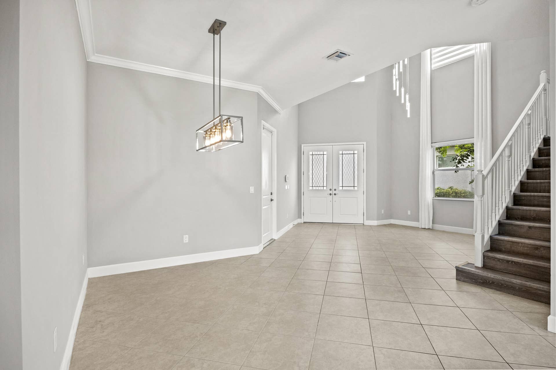 16007 Whippoorwill Circle, Westlake, Westlake, FL 33470 Expansive foyer with vaulted ceilings, tile flooring, a modern linear chandelier, and a prominent staircase with wood-finish treads