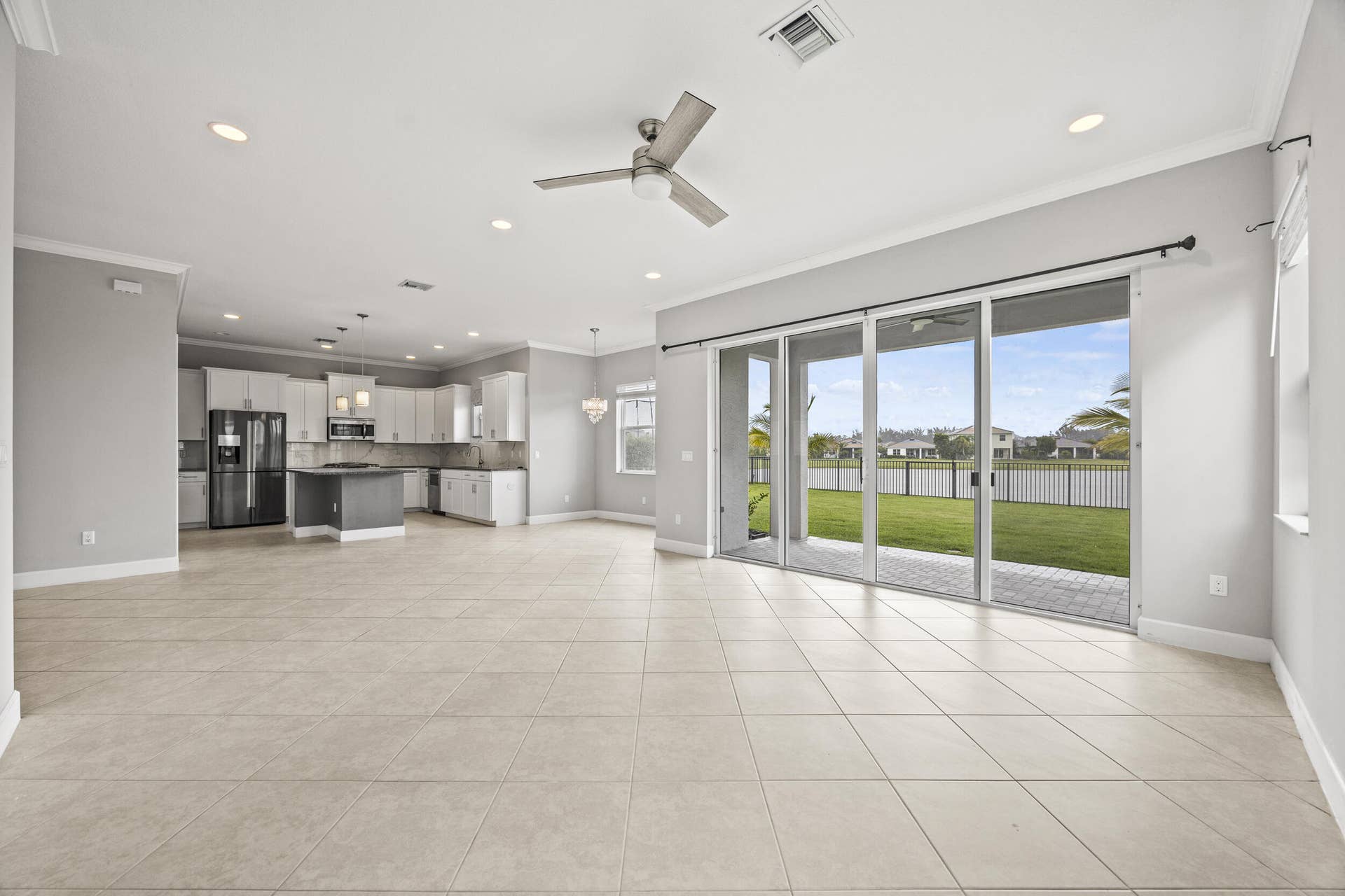 16007 Whippoorwill Circle, Westlake, Westlake, FL 33470 Open-concept living space featuring tiled flooring, a modern kitchen with a central island, and sliding glass doors leading to a paved patio