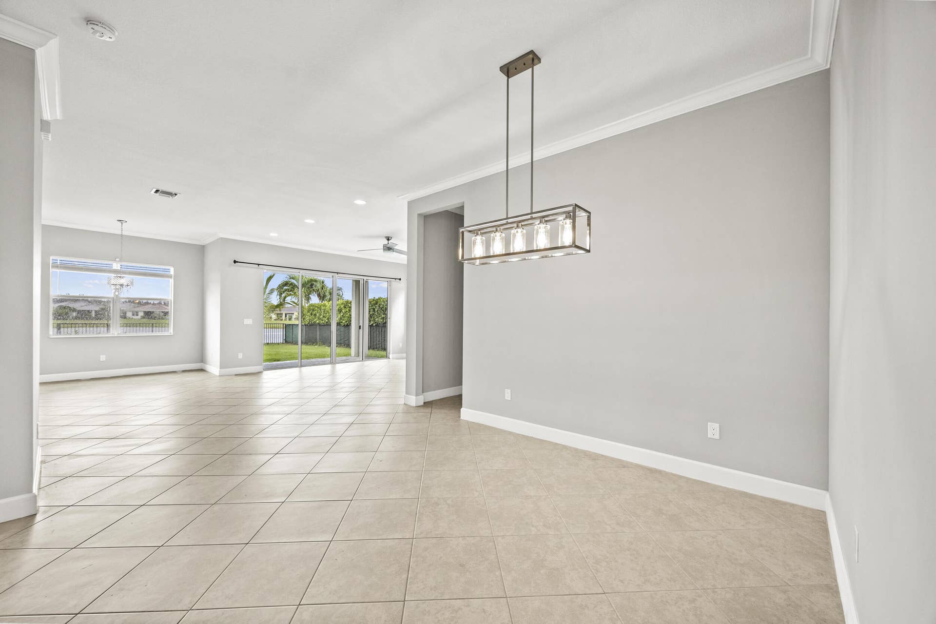 16007 Whippoorwill Circle, Westlake, Westlake, FL 33470 Open-concept interior featuring tile flooring, crown molding, a modern linear chandelier, and sliding glass doors opening to a backyard with water access