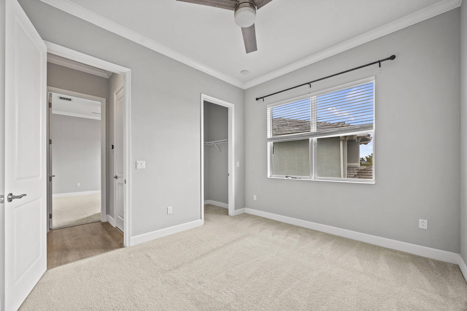 16007 Whippoorwill Circle, Westlake, Westlake, FL 33470 Bright secondary bedroom showcasing neutral gray walls, neutral carpet flooring, abundant natural light from large dual-pane windows, ceiling fan, and direct access to an ensuite bathroom with white cabinetry