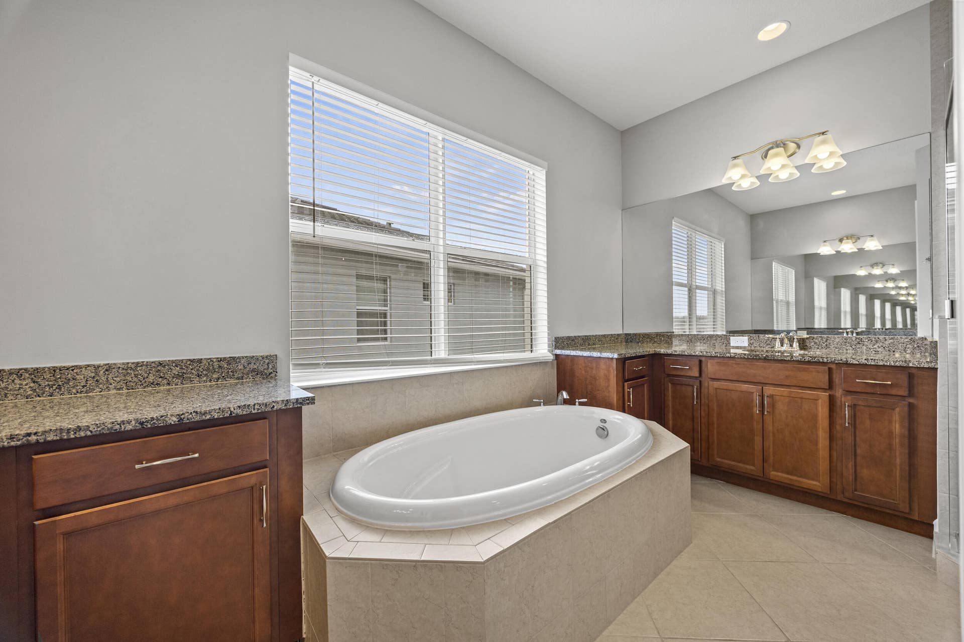 16007 Whippoorwill Circle, Westlake, Westlake, FL 33470 Soaking tub set within a tiled surround, dual wood-finish vanities with stone countertops, and a large mirror