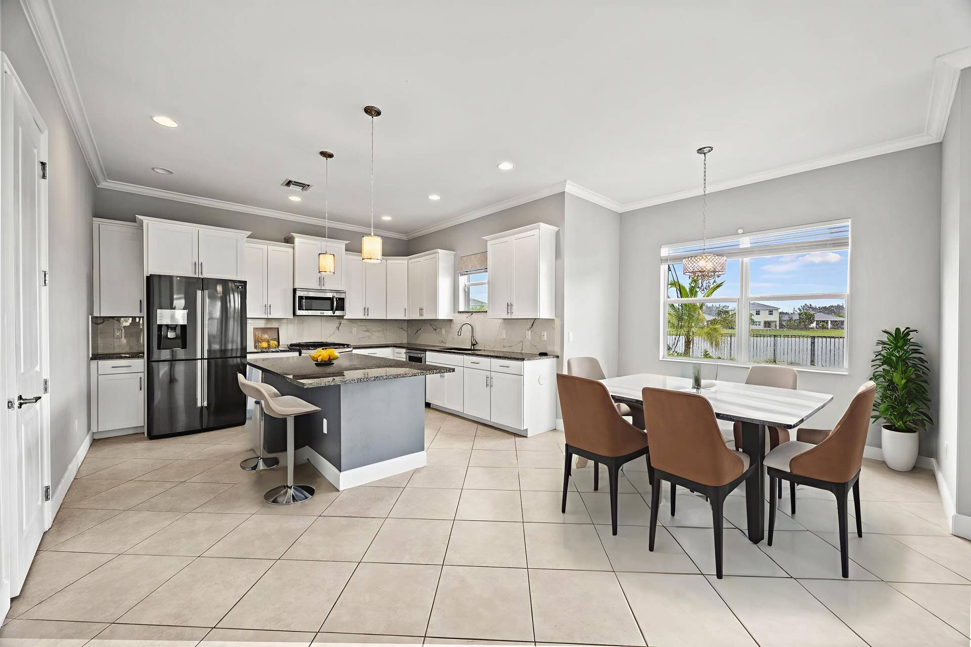 16007 Whippoorwill Circle, Westlake, Westlake, FL 33470 Open-concept kitchen and dining area featuring white cabinetry, stainless steel appliances including a French-door refrigerator, a center island with seating, tile flooring throughout, recessed lighting, and expansive windows showcasing outdoor scenery
