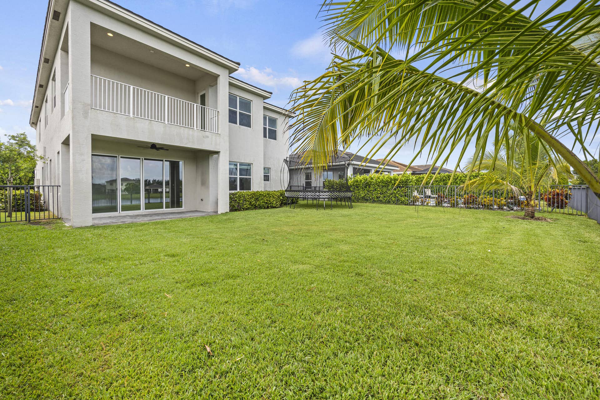 16007 Whippoorwill Circle, Westlake, Westlake, FL 33470 Expansive rear lawn, covered patio, second-story balcony with white railings, and large sliding glass doors