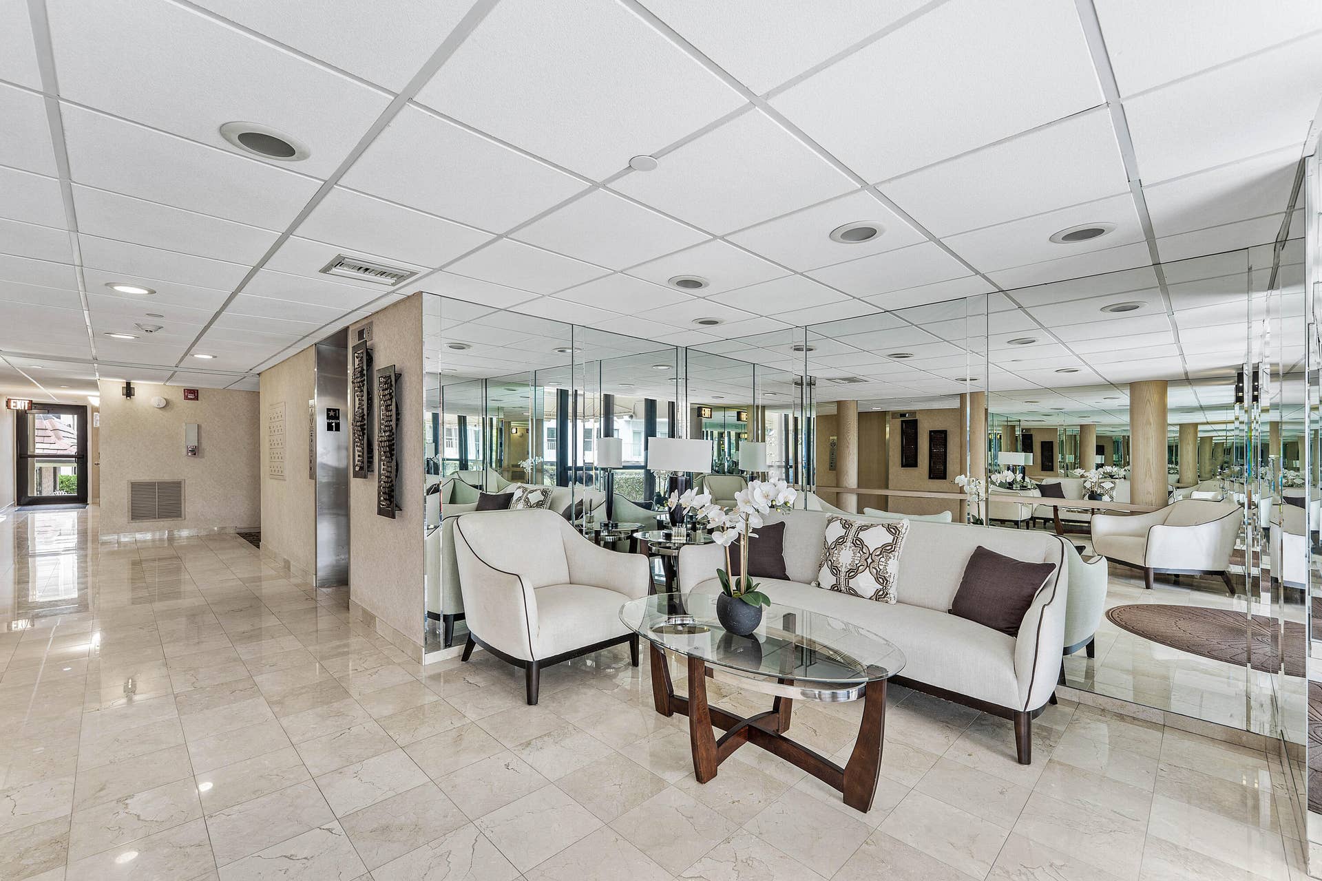 Spacious common area featuring large format tile flooring, mirrored wall accents, recessed lighting, and a suspended acoustic tile ceiling