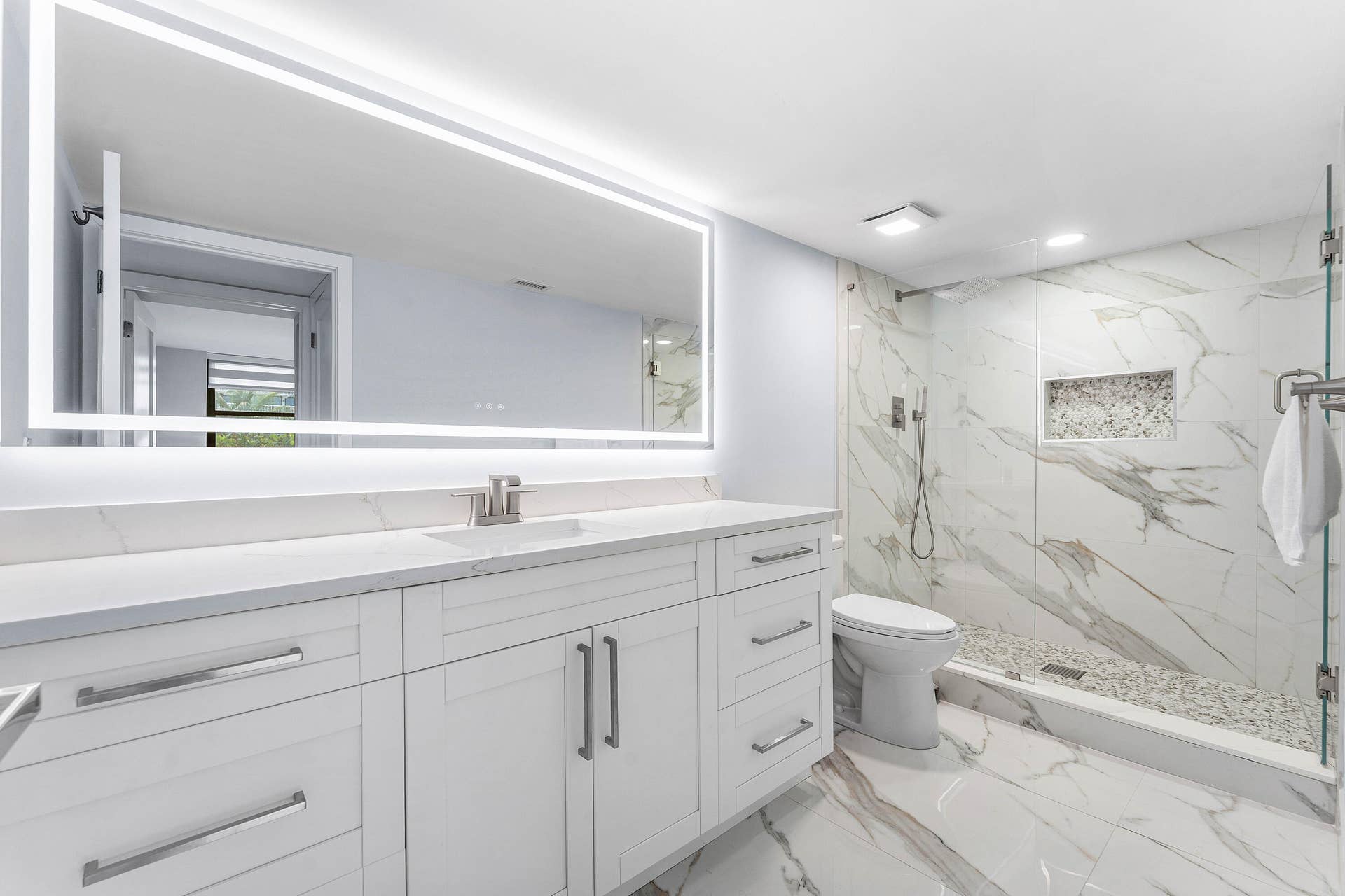 Fully renovated vanity with white shaker cabinetry, stunning large all tile and glass shower and a large illuminated mirror