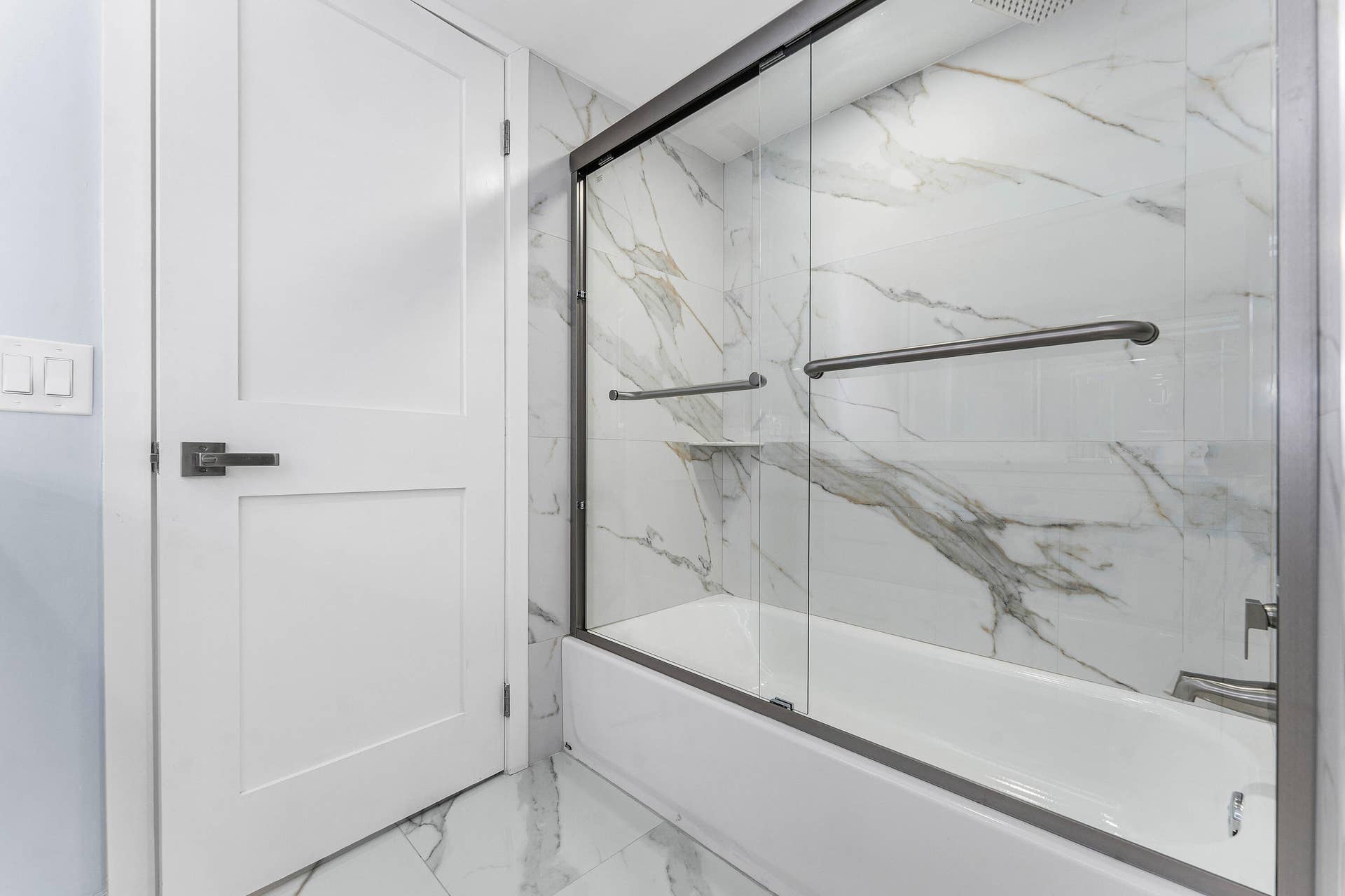 Bathtub with glass enclosure, wall tiling, and coordinating floor tiles.