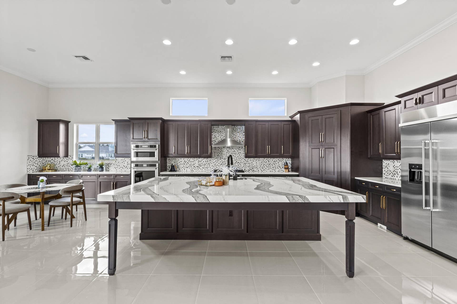 14976 Woodlot Court, Westlake, FL 33470 Expansive kitchen featuring a large central island with a decorative countertop, dark wood-finish cabinetry, stainless steel appliances, and tile flooring