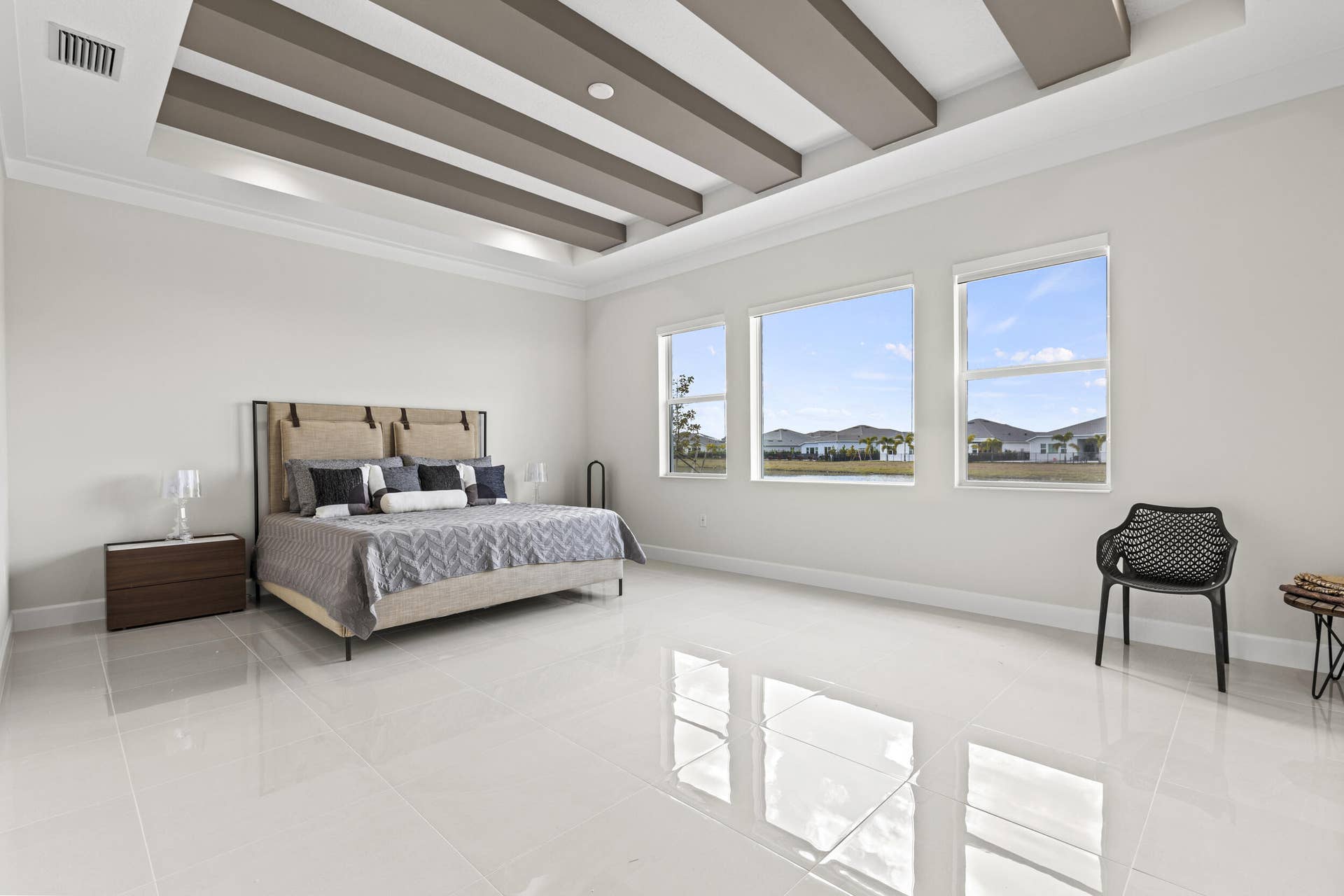 14976 Woodlot Court, Westlake, FL 33470 Owner's Suite featuring tray ceiling with decorative beams, large windows, light-toned flooring, and a spacious layout