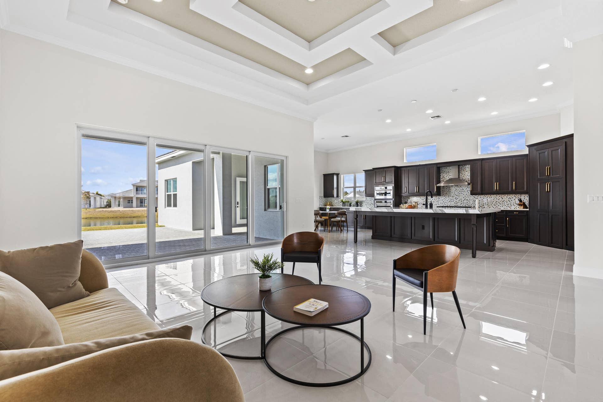 14976 Woodlot Court, Westlake, FL 33470 Open-concept living and kitchen area featuring polished light-finish flooring, coffered ceiling with recessed lighting, and expansive sliding glass doors opening to outdoor space