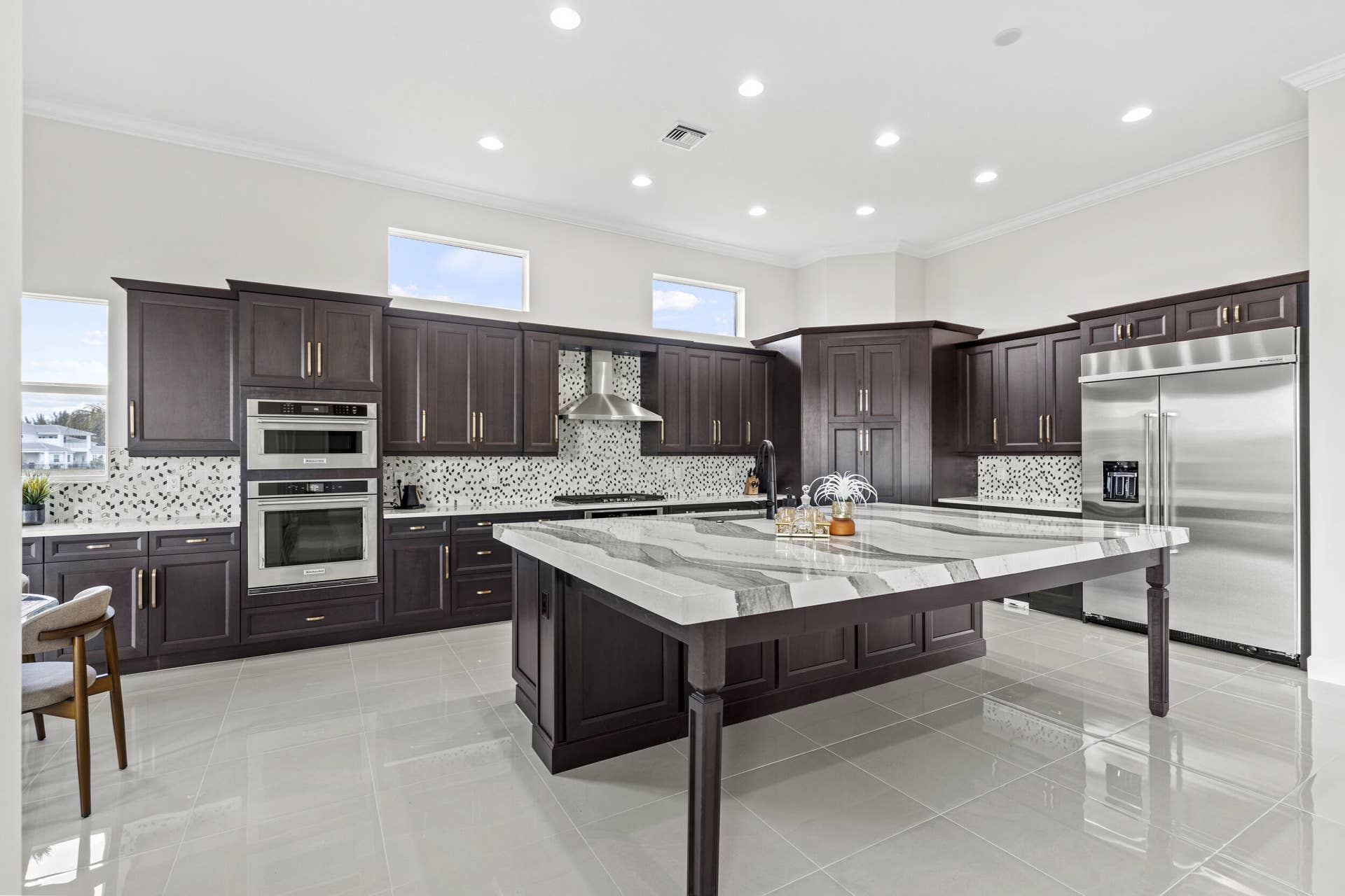 14976 Woodlot Court, Westlake, FL 33470 Spacious kitchen featuring dark wood cabinetry, a large kitchen island with a light-toned countertop, stainless steel appliances, and tile flooring