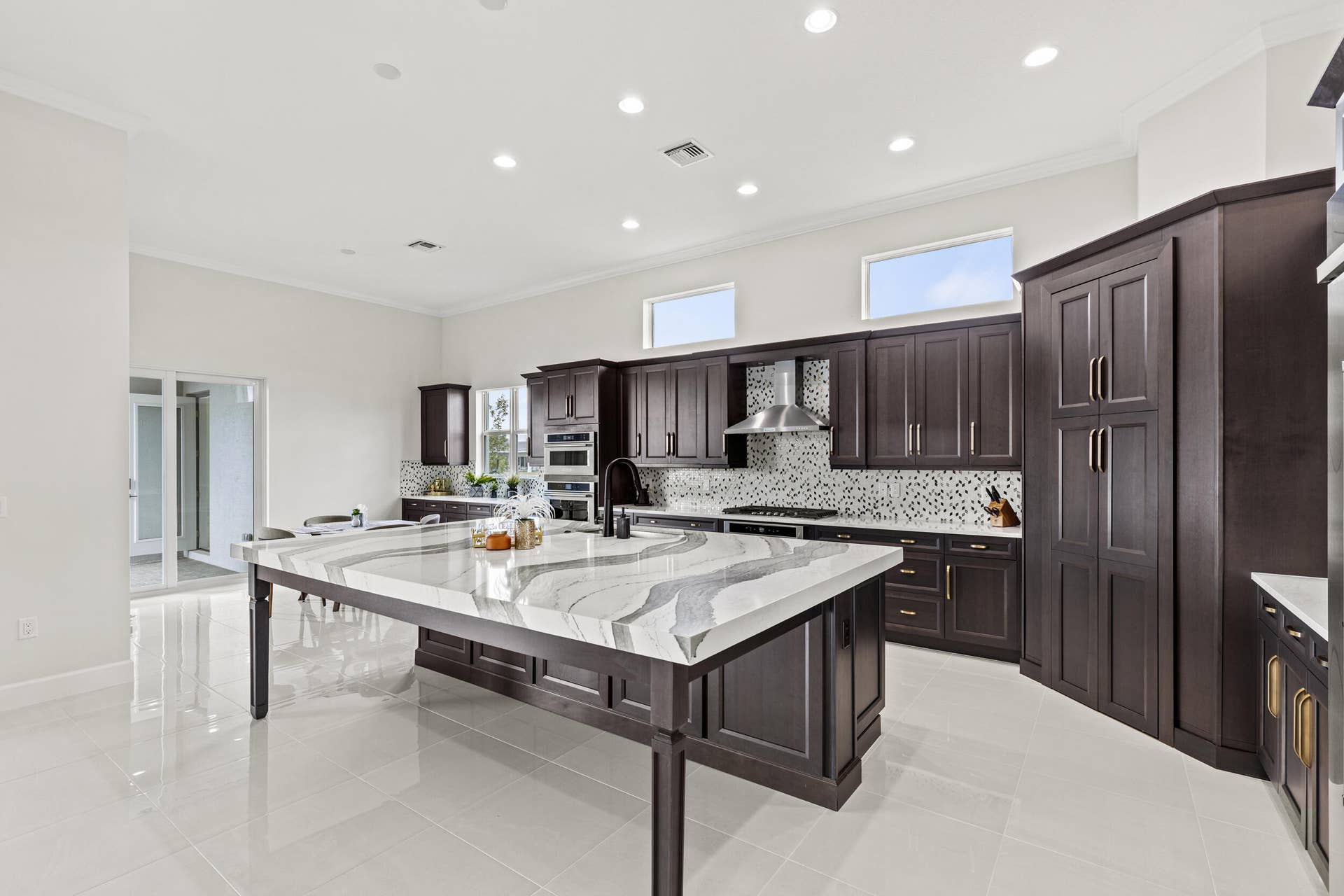 14976 Woodlot Court, Westlake, FL 33470 Kitchen featuring dark wood-finish cabinetry, a large center island with a unique veined countertop, mosaic tile backsplash, stainless steel range hood, and recessed lighting