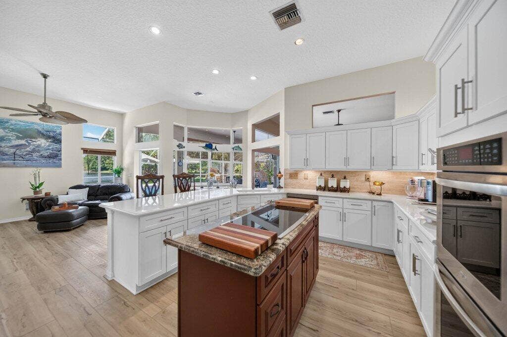 Gourmet kitchen featuring a large central island, white shaker cabinetry, stainless steel appliances, and light wood-finish flooring