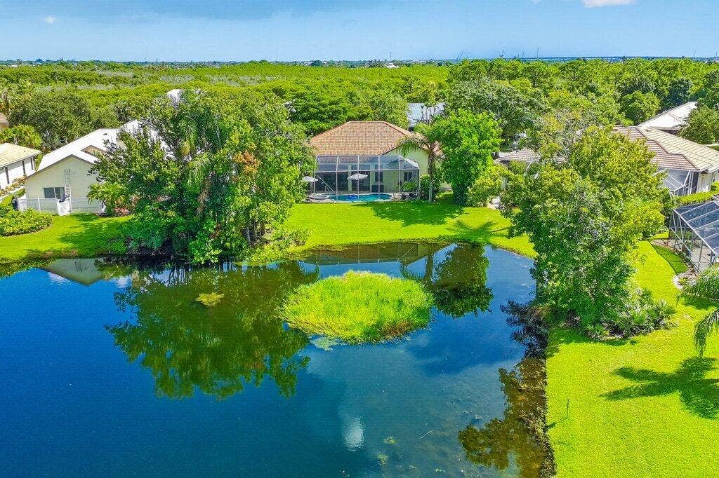 Lush green landscaping with mature trees, a private pool, and a screened patio enclosure