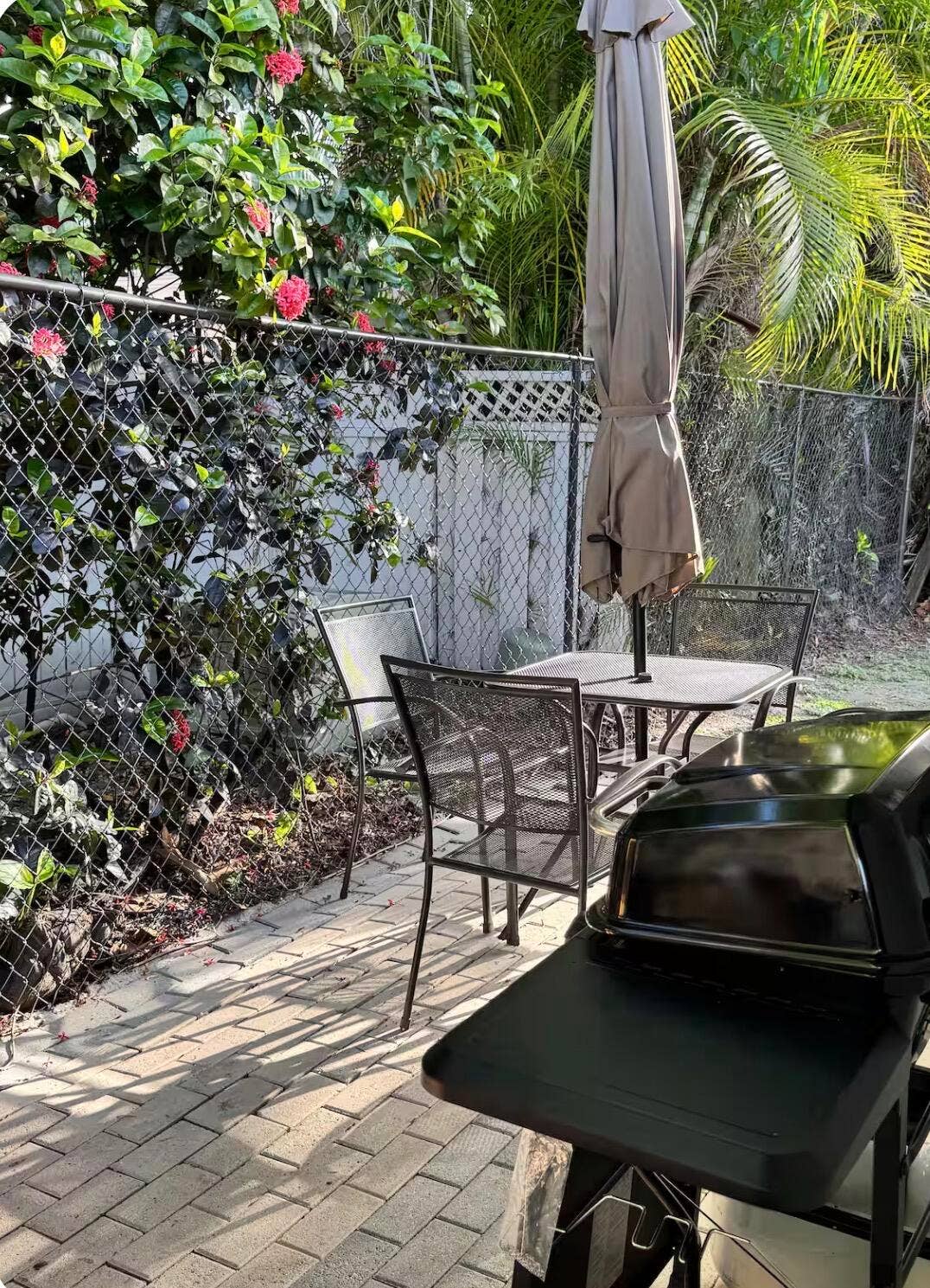 patio with lush tropical landscaping, brick pavers, outdoor dining area, and grill.