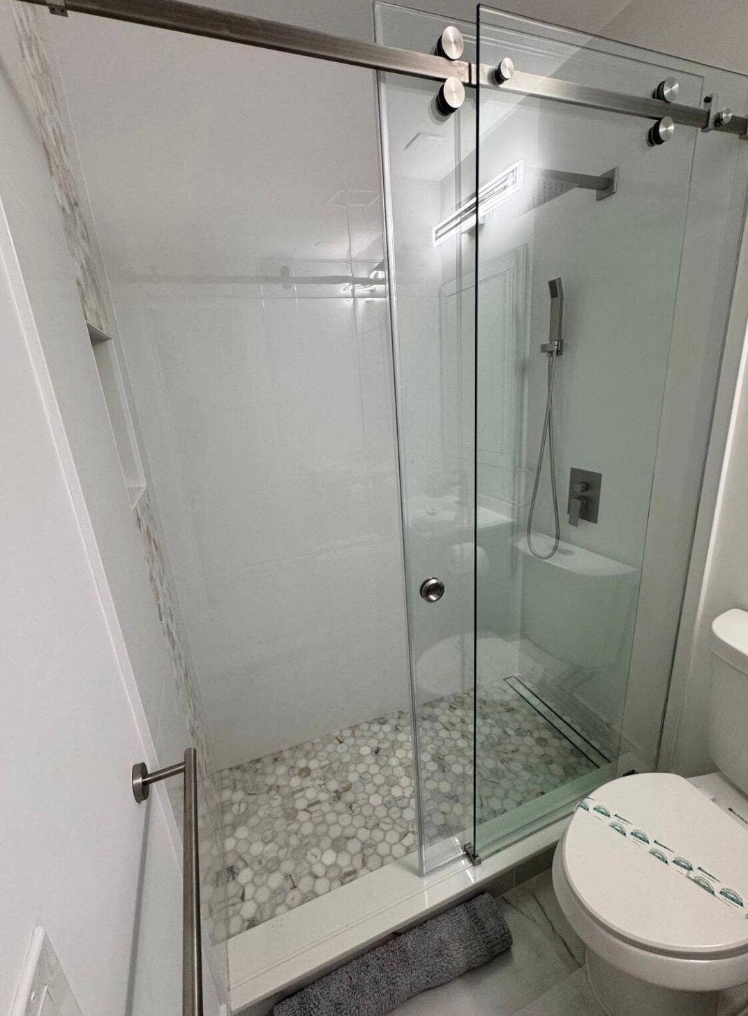 Frameless glass shower enclosure with sliding door, pebble tile shower floor, and a linear shower drain
