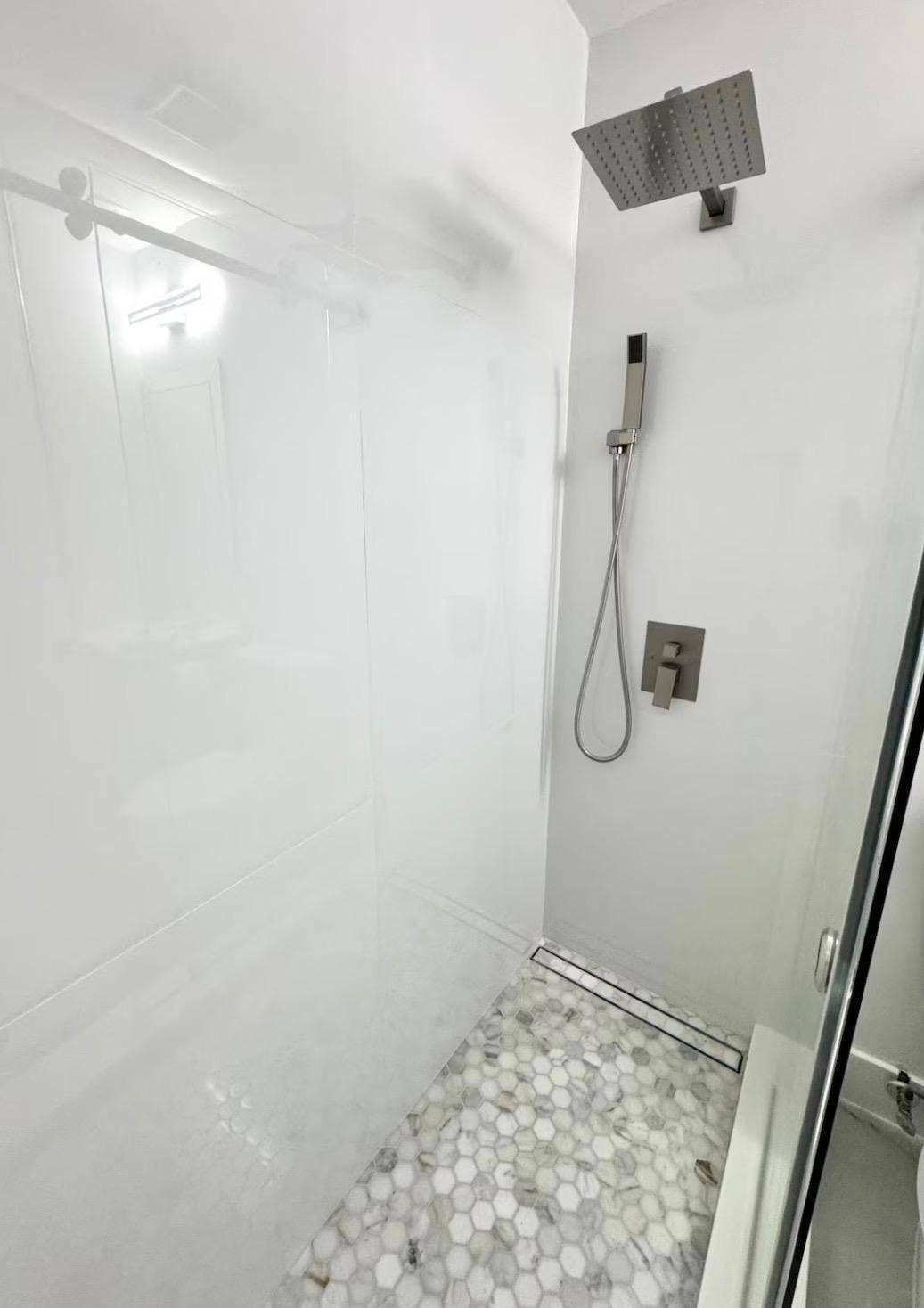 Walk-in shower with hexagonal floor tile, linear drain, and a rain showerhead with an additional handheld shower fixture