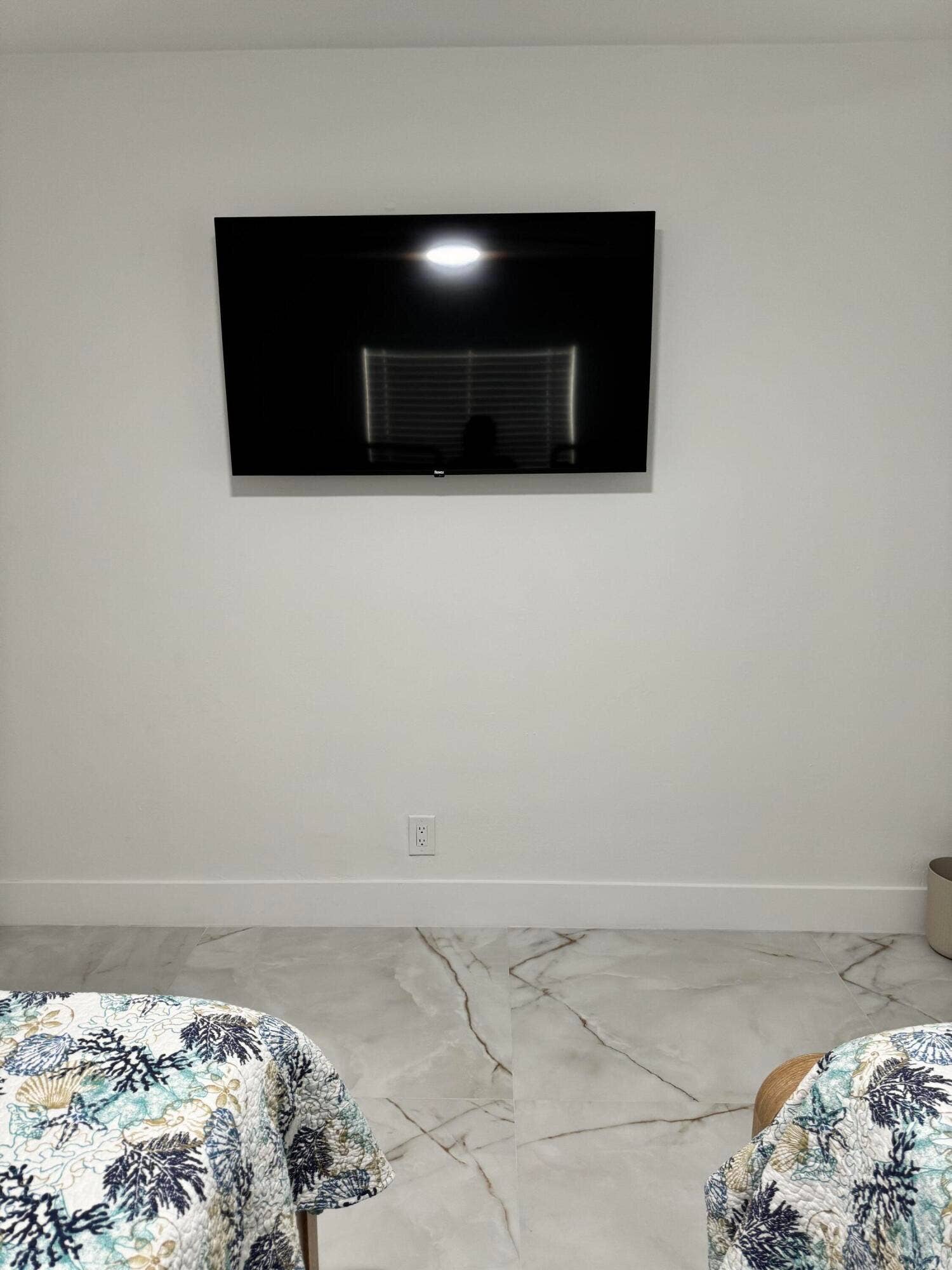 Spacious bedroom featuring a wall-mounted TV, elegant marble-look tile flooring, and a clean, modern design