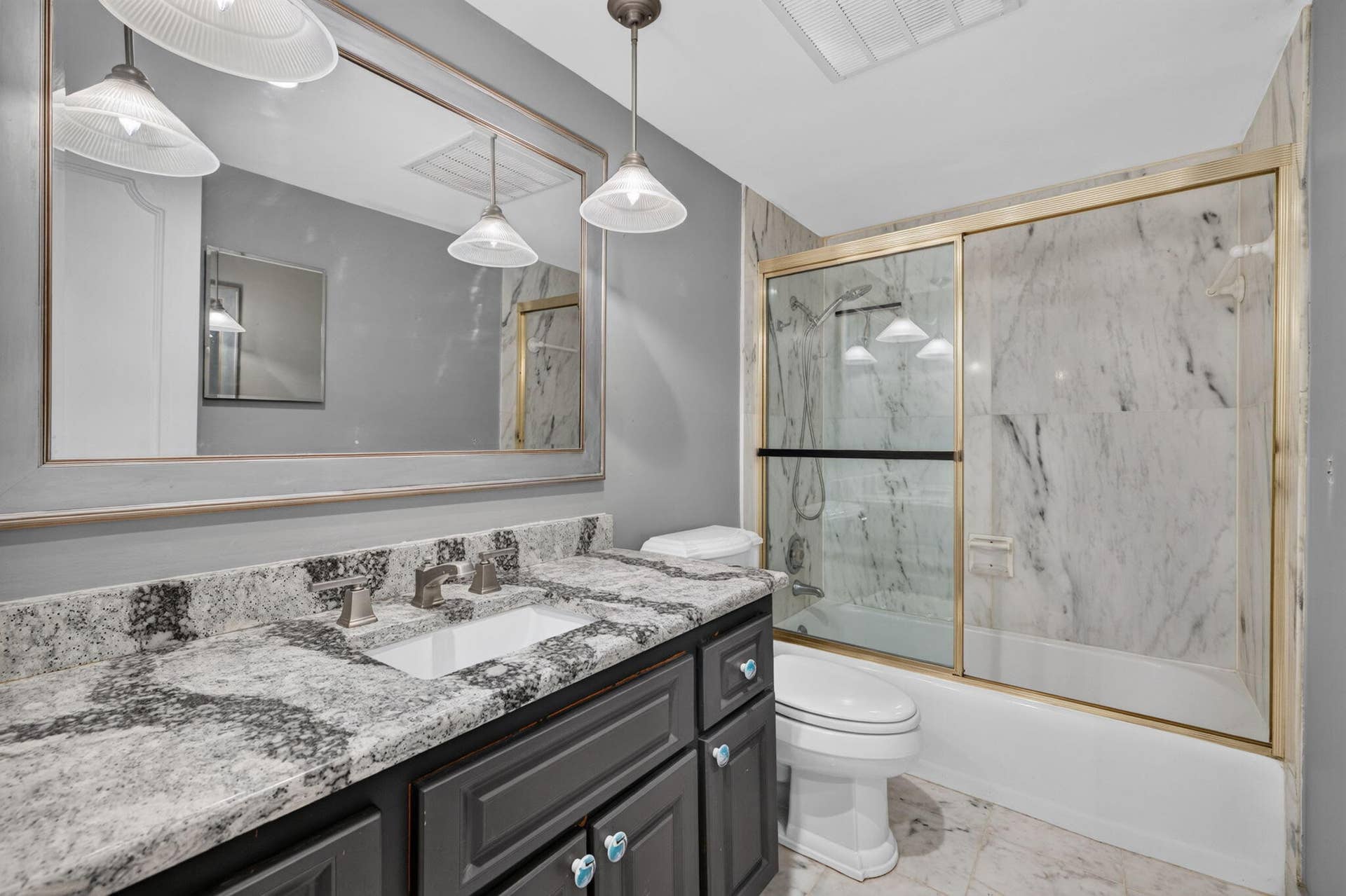 Granite countertop with integrated sink, dark wood-finish vanity, large framed mirror, glass-enclosed shower with tiled walls, and recessed ceiling lighting