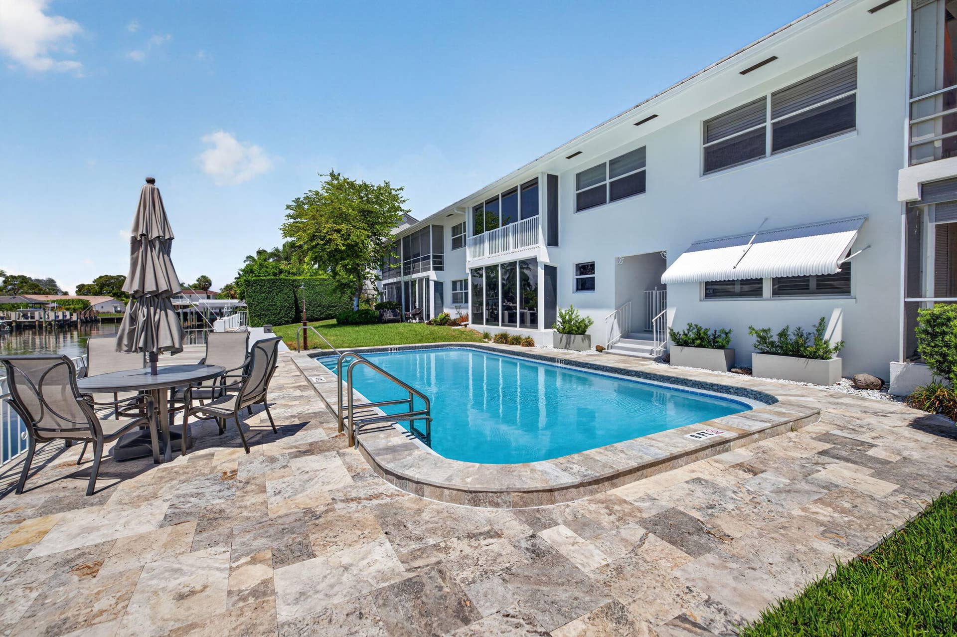 Waterfront property featuring a swimming pool, stone patio, manicured lawn, and white exterior