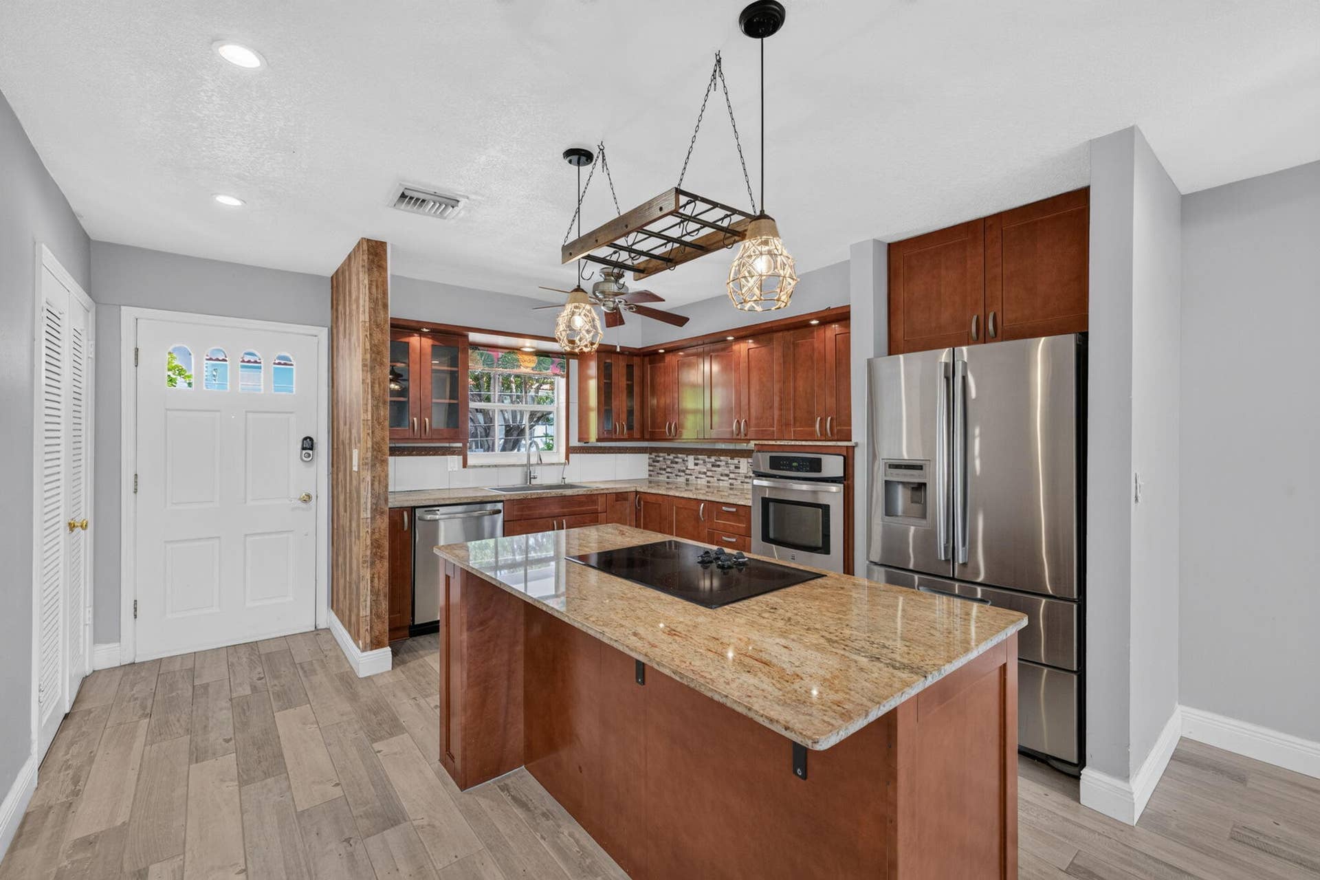 Kitchen featuring wood-finish flooring, an island with an integrated cooktop, stainless steel appliances, wood cabinetry, and a mosaic tile backsplash