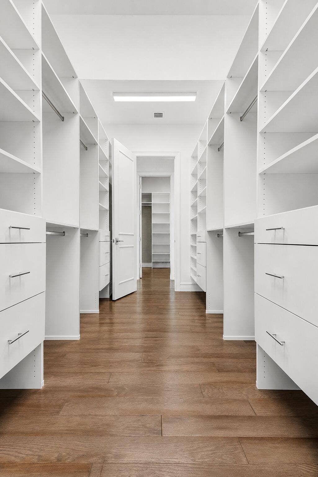 9046 CHAUVET Way, Boca Raton, FL 33496 Spacious walk-in closet featuring extensive white shelving, built-in drawers with modern hardware, hanging rods, and wood-finish flooring