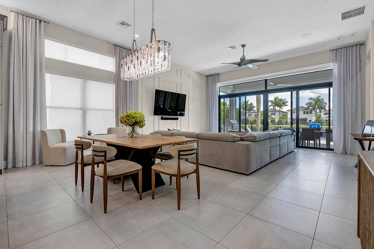9046 CHAUVET Way, Boca Raton, FL 33496 Spacious interior featuring large format tile flooring, a contemporary chandelier, a decorative accent wall, floor-to-ceiling windows with roller shades, and expansive sliding glass doors leading to an outdoor area