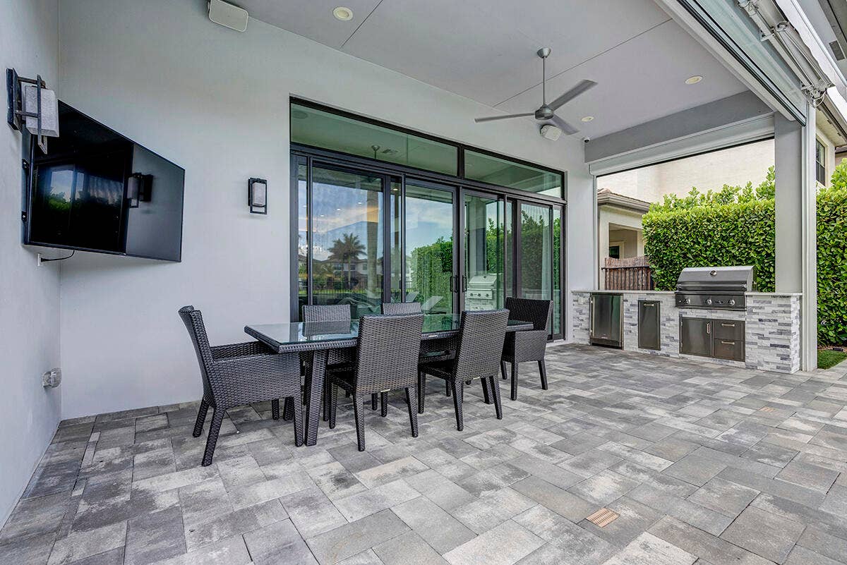 9046 CHAUVET Way, Boca Raton, FL 33496 Expansive outdoor patio featuring gray paver flooring and an integrated outdoor kitchen with stainless steel appliances and stone veneer detailing