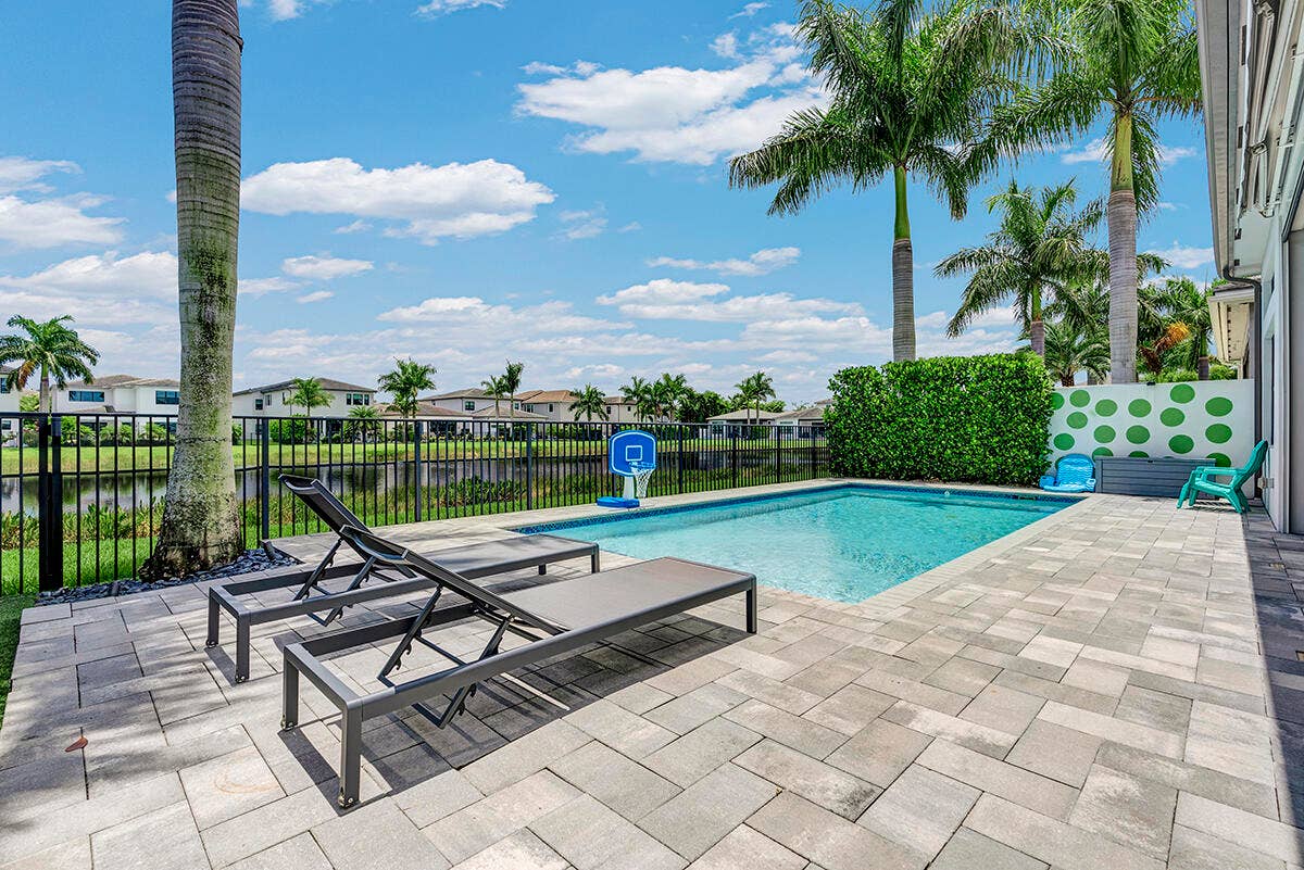 9046 CHAUVET Way, Boca Raton, FL 33496 Private swimming pool with paver patio, surrounded by lush landscaping and a black wrought-iron fence