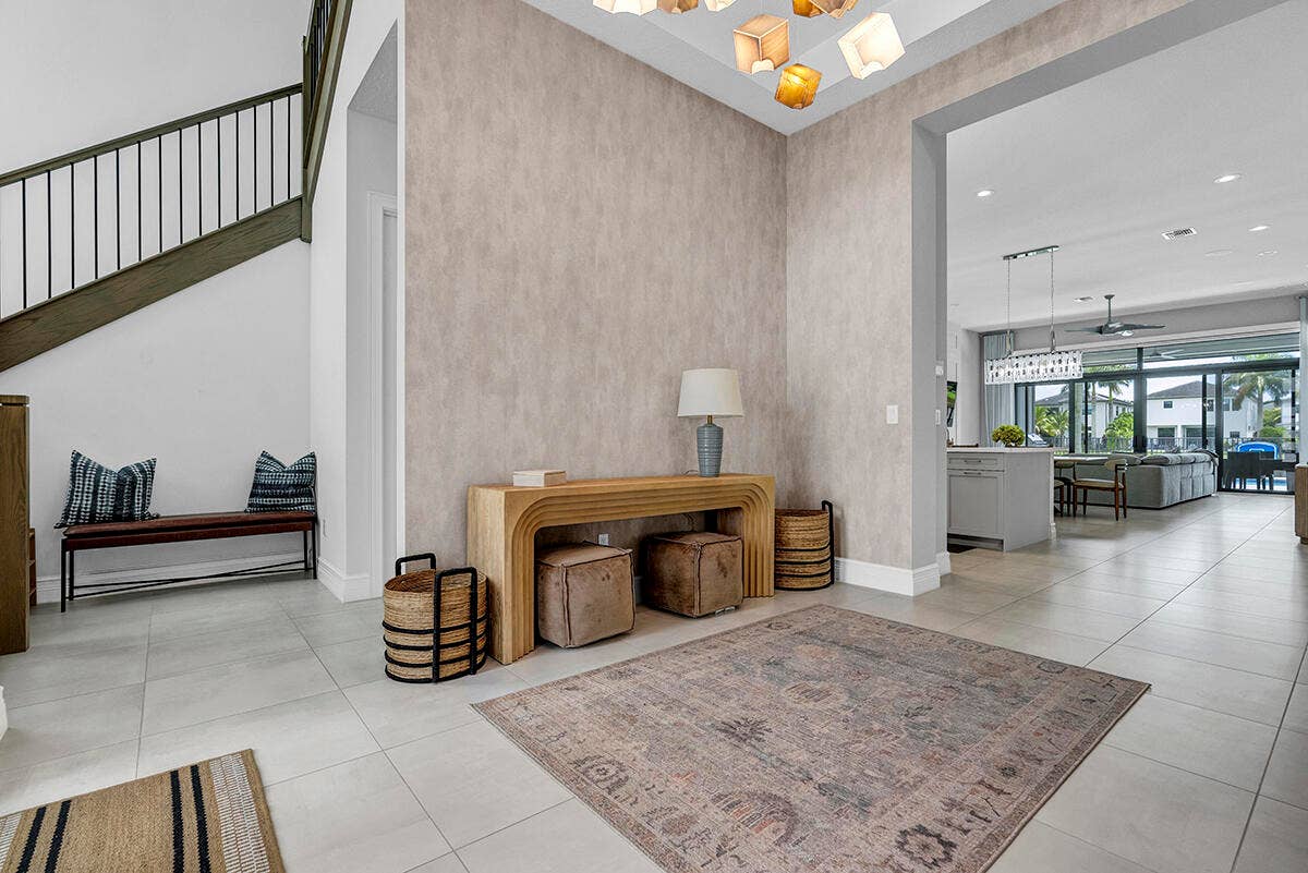 9046 CHAUVET Way, Boca Raton, FL 33496 Spacious foyer featuring light-toned tile flooring, a contemporary chandelier, a custom wood staircase with metal balusters, textured wall detailing, and an expansive archway leading to an open-concept interior