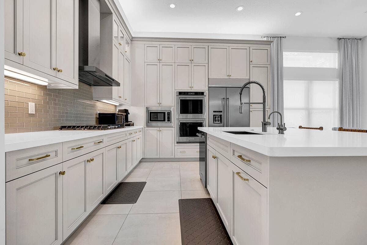 9046 CHAUVET Way, Boca Raton, FL 33496 Gourmet kitchen featuring extensive light cabinetry, light countertops, a large center island with an undermount sink, stainless steel appliances, and a subway tile backsplash