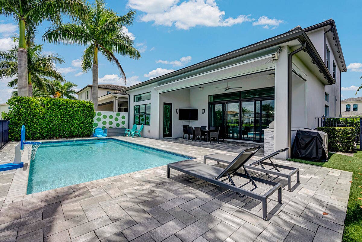 9046 CHAUVET Way, Boca Raton, FL 33496 Outdoor living area featuring a rectangular pool with paver decking, an expansive covered patio, large sliding glass doors, and mature palm trees