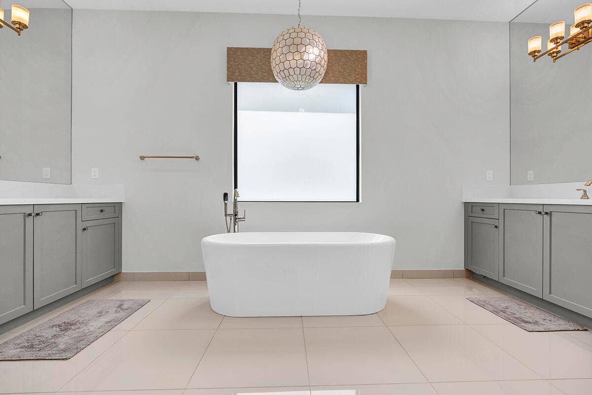 9046 CHAUVET Way, Boca Raton, FL 33496 Freestanding soaking tub with a floor-mounted faucet, flanked by dual vanities with gray cabinetry and white countertops