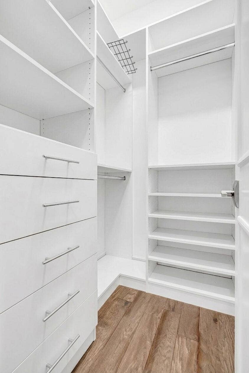 9046 CHAUVET Way, Boca Raton, FL 33496 Custom closet system featuring multiple hanging rods, built-in shelving, integrated drawers with brushed nickel pulls, a wire storage rack, and wood-finish flooring