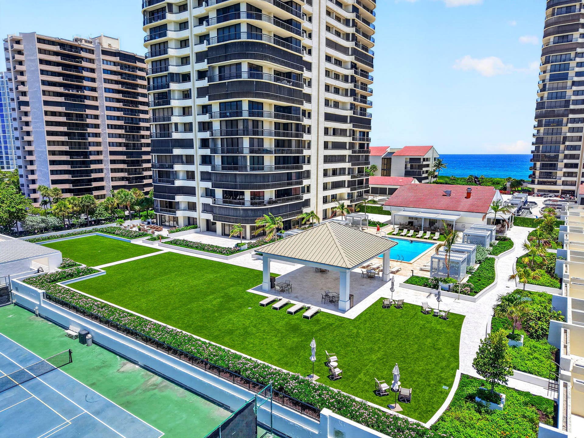 Elevated view of the resort-style pool deck showcases private cabana-style lounges, lush landscaping and generous space for relaxing in the Florida sun.