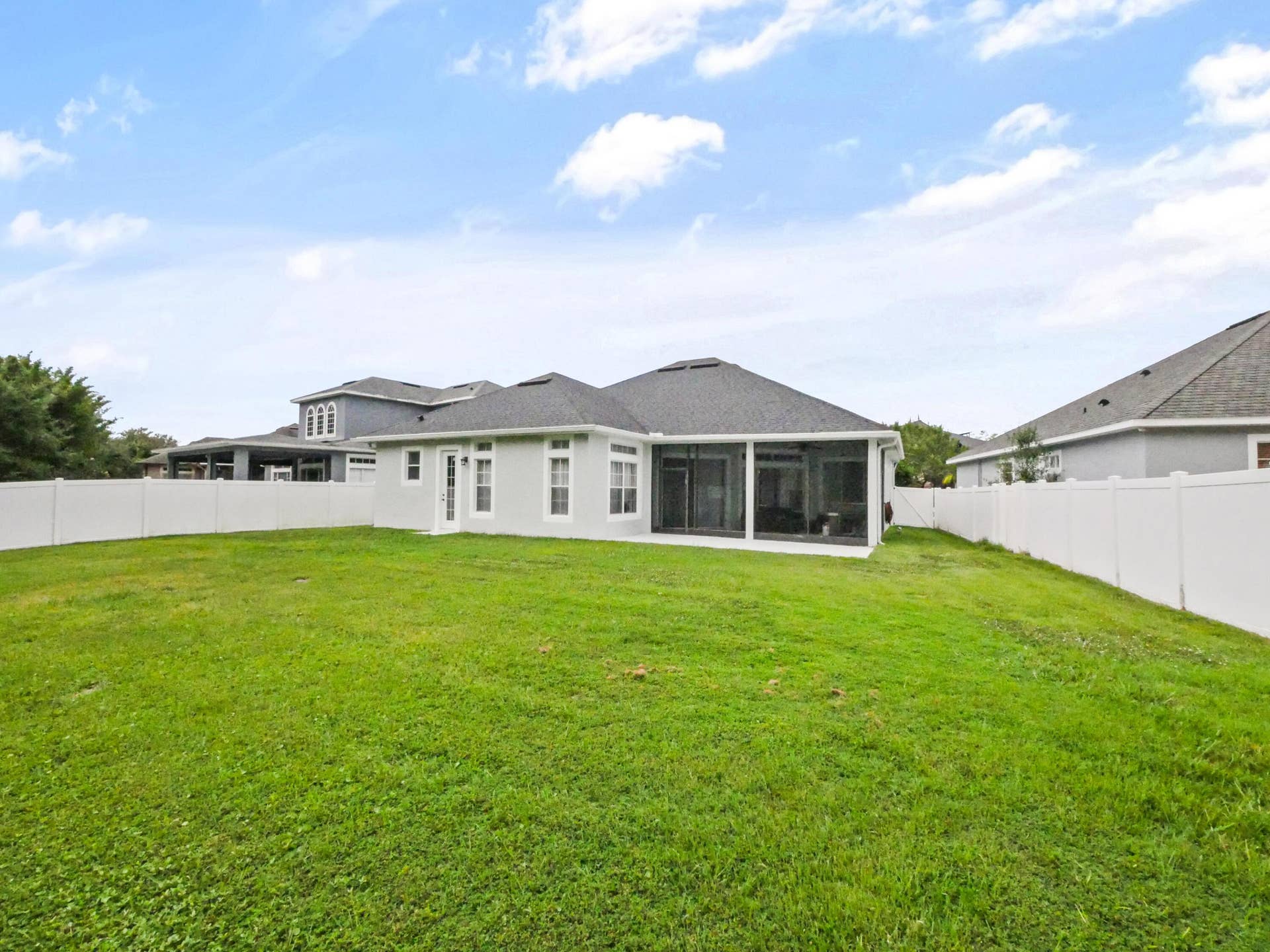 16437 TUDOR GROVE Drive, Orlando, FL 32828 Expansive backyard featuring a manicured lawn, a full white privacy fence, and a screened-in lanai