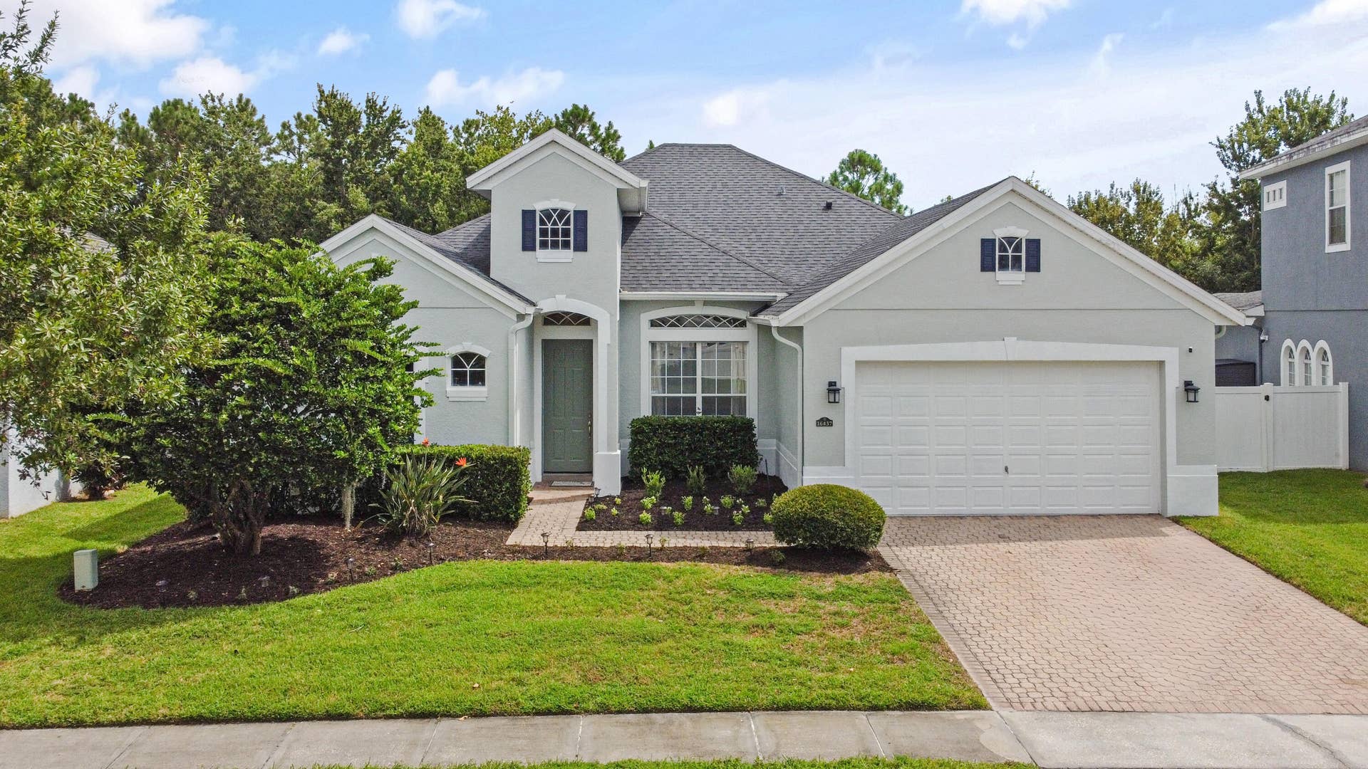 16437 TUDOR GROVE Drive, Orlando, FL 32828 Stucco exterior with a dark shingle roof, arched entryway, a paver driveway, and an attached two-car garage