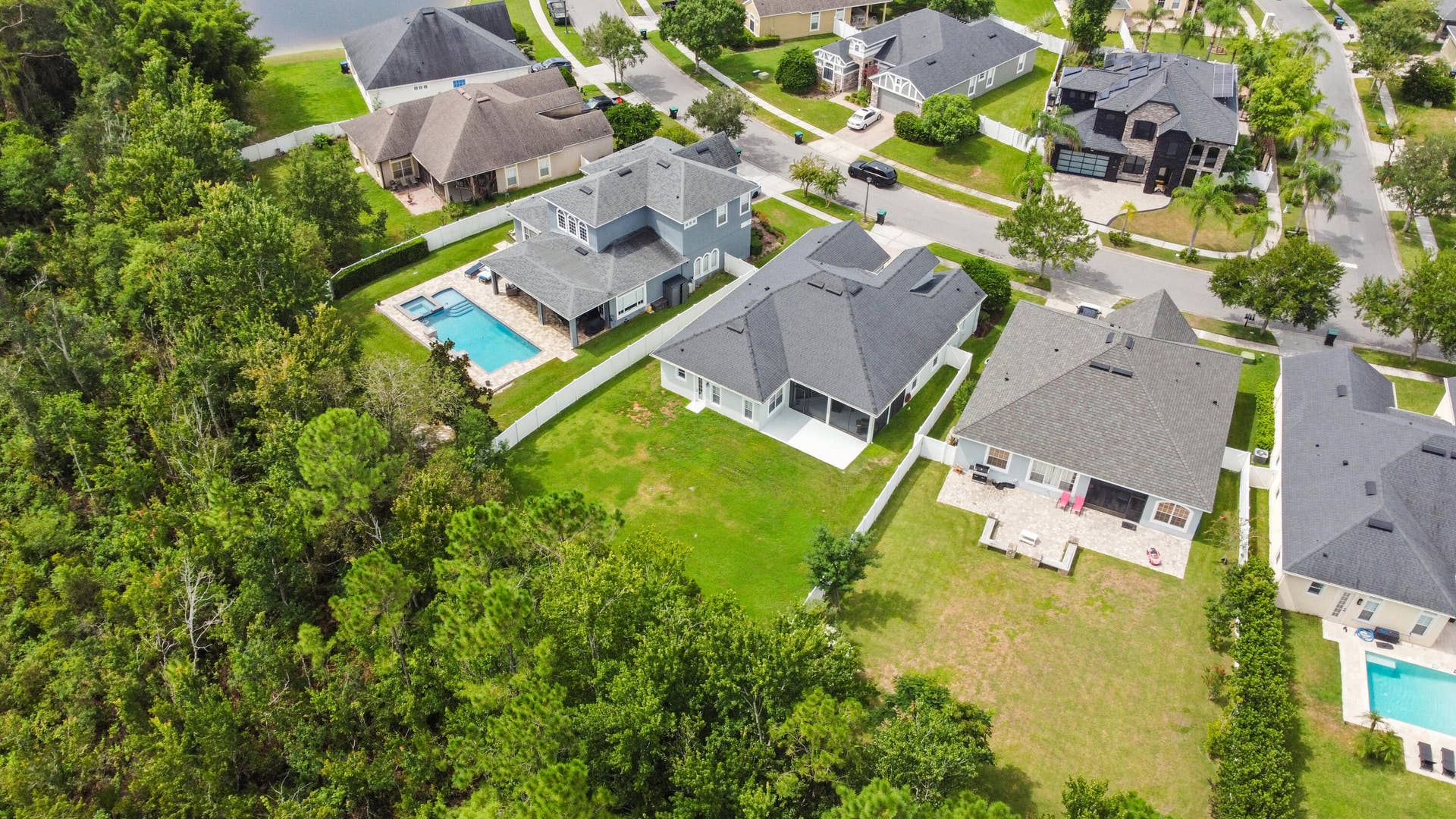 16437 TUDOR GROVE Drive, Orlando, FL 32828 Lush green surroundings with mature trees, expansive backyard with a manicured lawn, private swimming pool with integrated spa, covered patio space, and a well-maintained neighborhood setting
