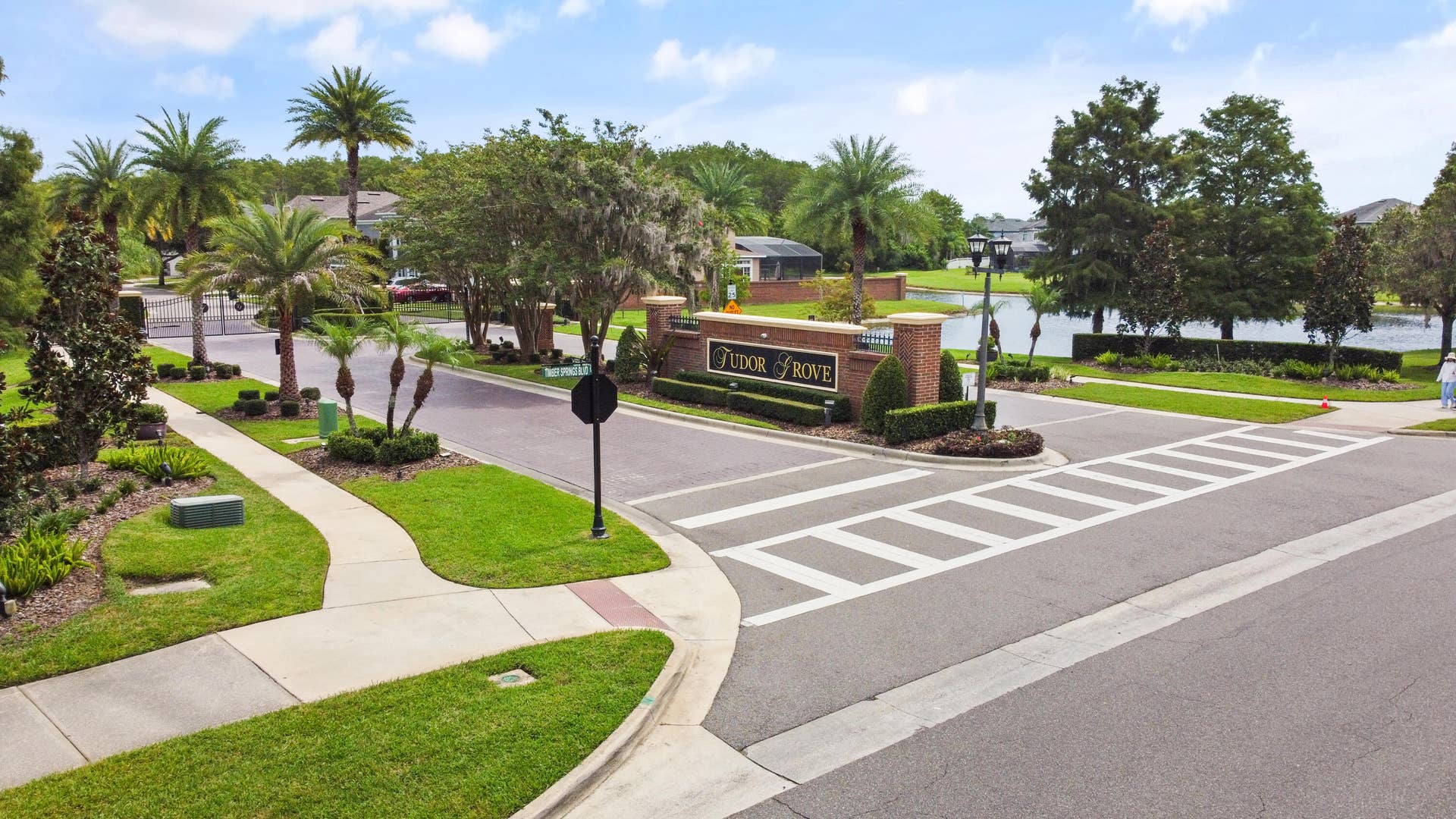 16437 TUDOR GROVE Drive, Orlando, FL 32828 Community entrance with brick monument sign, mature landscaping, paved streets, sidewalks, and water feature
