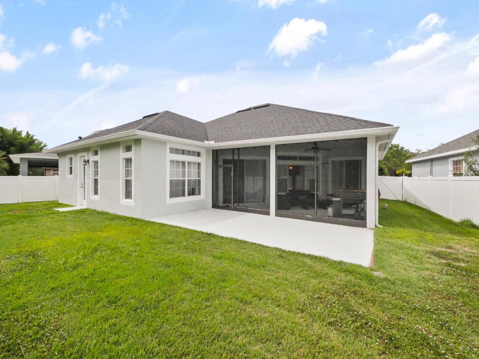 16437 TUDOR GROVE Drive, Orlando, FL 32828 Expansive backyard featuring a manicured lawn, concrete patio, screened lanai, and white vinyl perimeter fencing