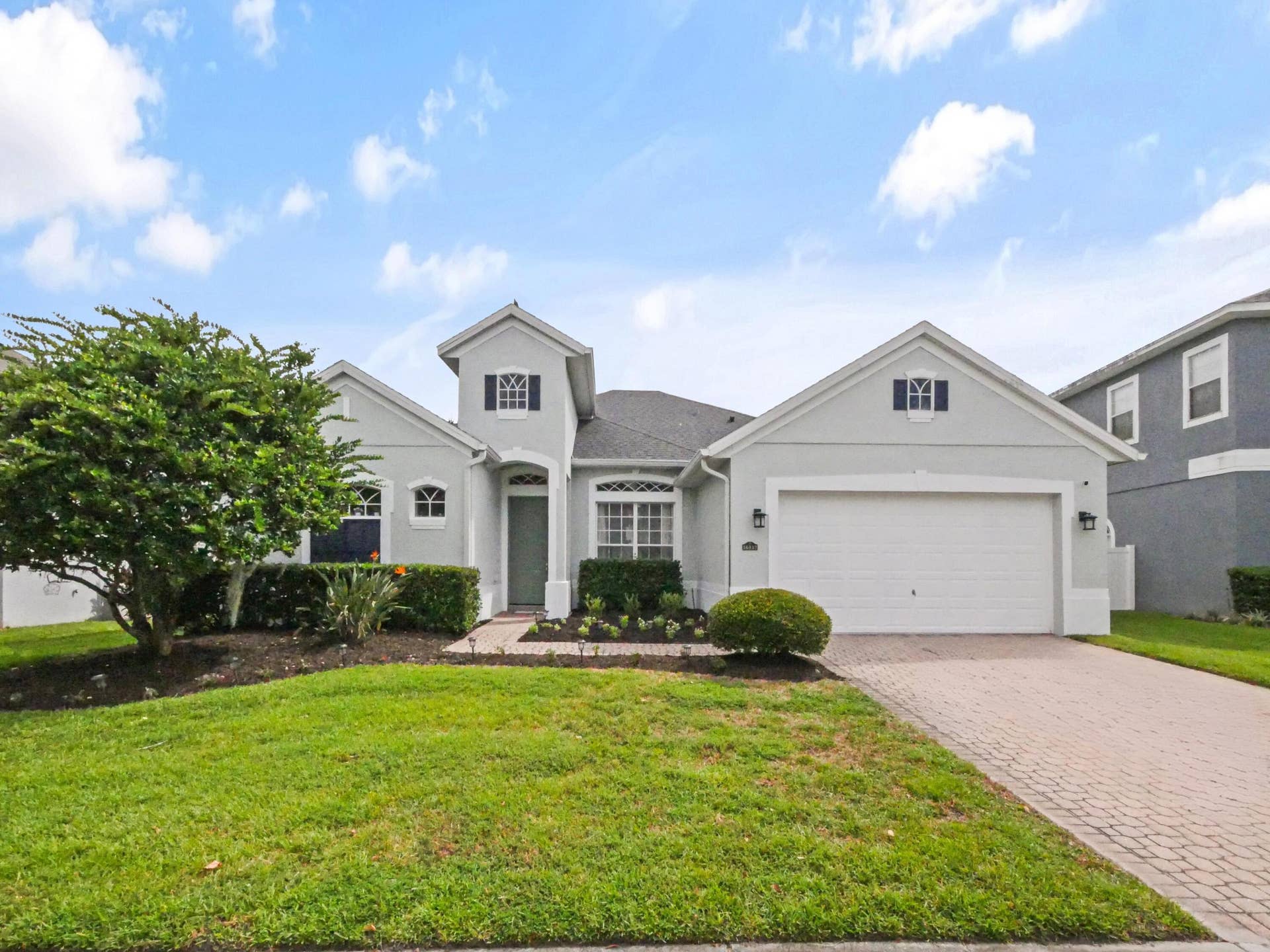 16437 TUDOR GROVE Drive, Orlando, FL 32828 Stucco exterior with a peaked roofline, arched entry, paver driveway, attached garage, and manicured landscaping