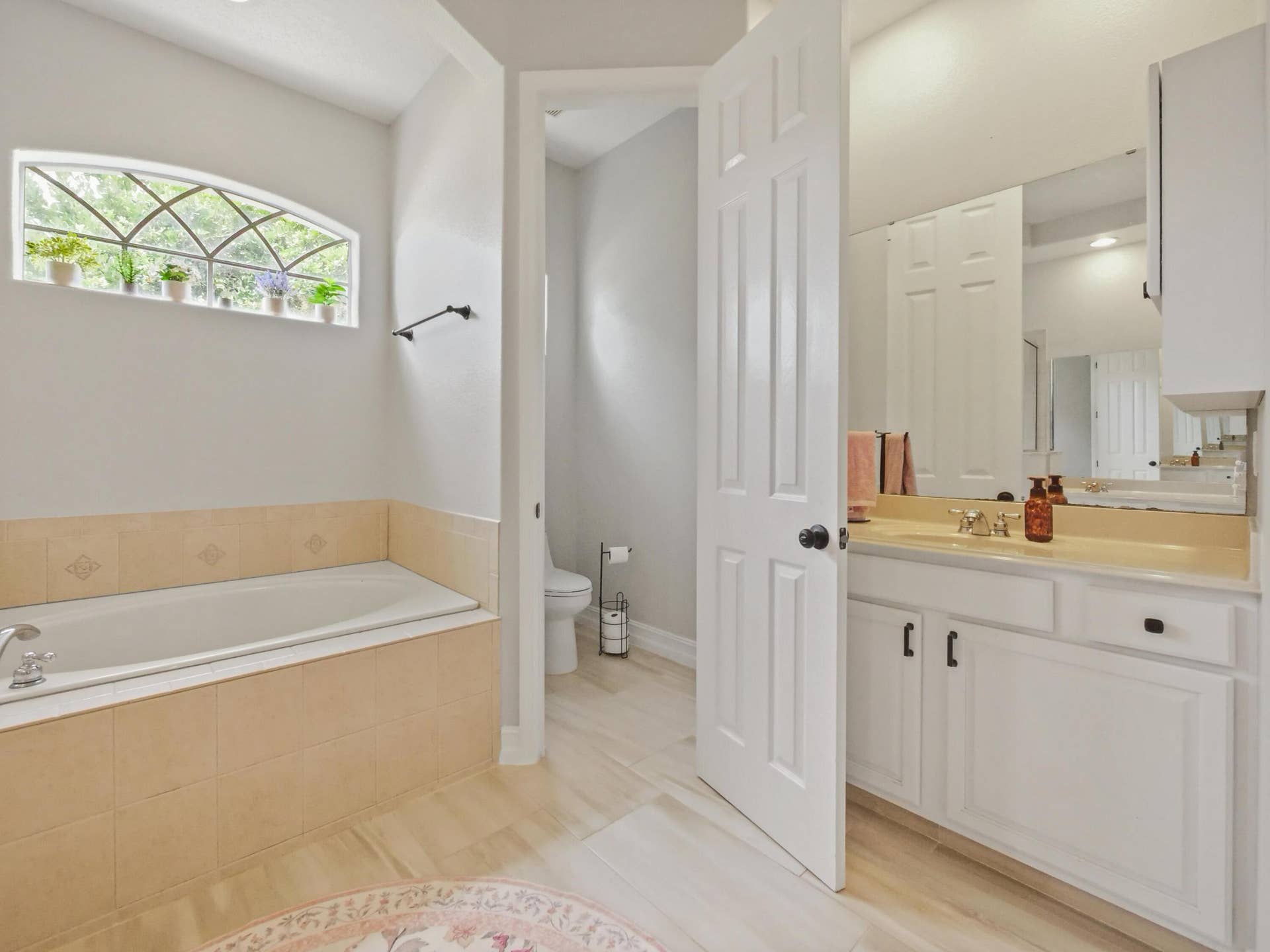 16437 TUDOR GROVE Drive, Orlando, FL 32828 Soaking tub with tiled surround, arched window, single vanity with integrated sink, wall-mounted mirror, and white paneled cabinetry