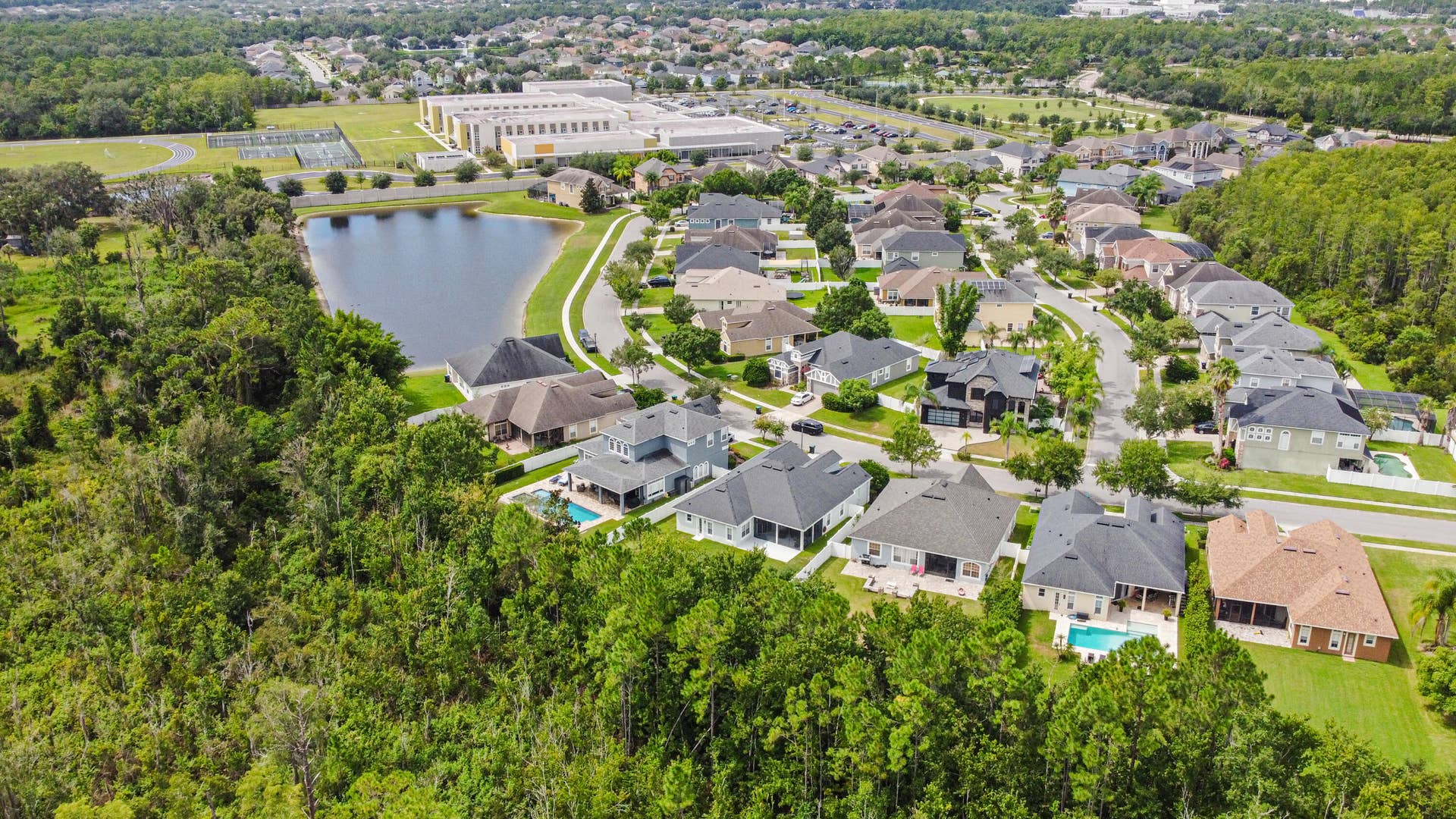 16437 TUDOR GROVE Drive, Orlando, FL 32828 Residential community featuring single-family homes, mature landscaping, a central pond, and proximity to a large educational facility with sports fields