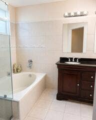18431 NW 18TH Street, Pembroke Pines, FL 33029 Enclosed soaking tub with wall-mounted fixtures, glass shower enclosure, wood-finish vanity with an undermount sink, dark countertop, and tiled flooring