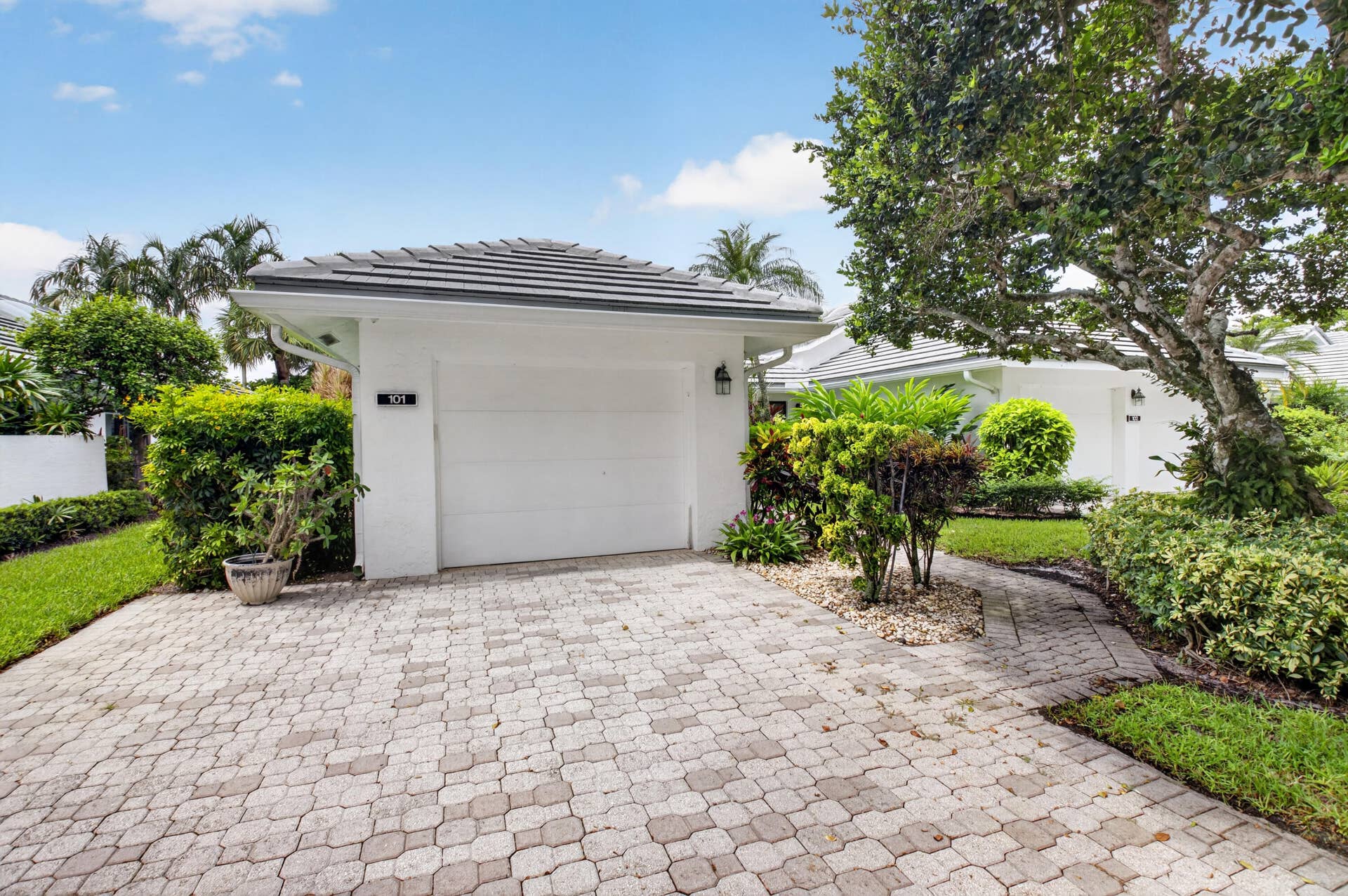 20065 Waters Edge Drive, #101, Boca Raton, FL 33434 Paver driveway and walkway, lush landscaping, white exterior, garage with white door, gray tile roof