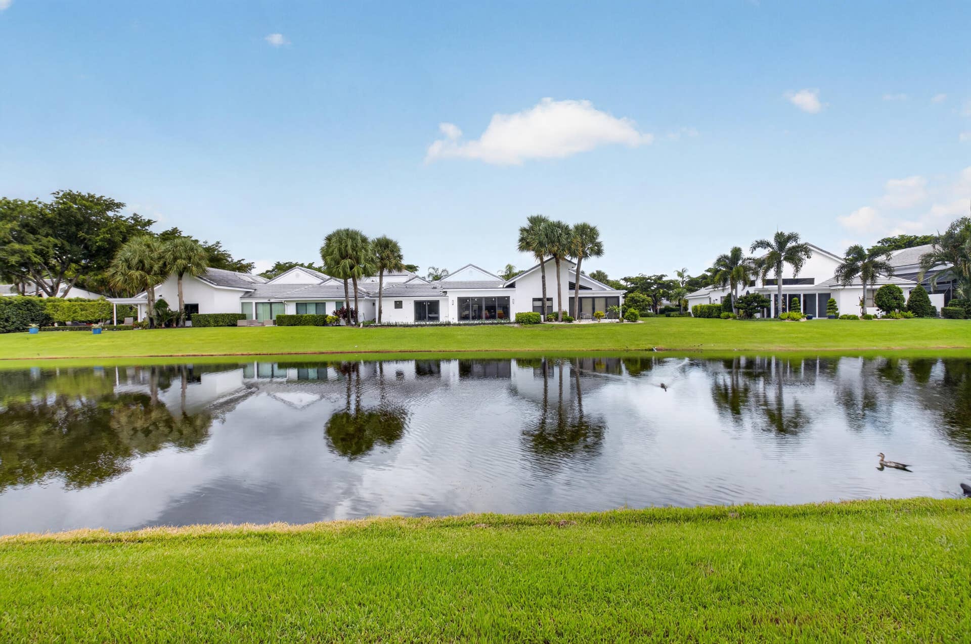 20065 Waters Edge Drive, #101, Boca Raton, FL 33434 Lakeside property featuring a manicured lawn, established palm trees, and a white exterior with multiple windows