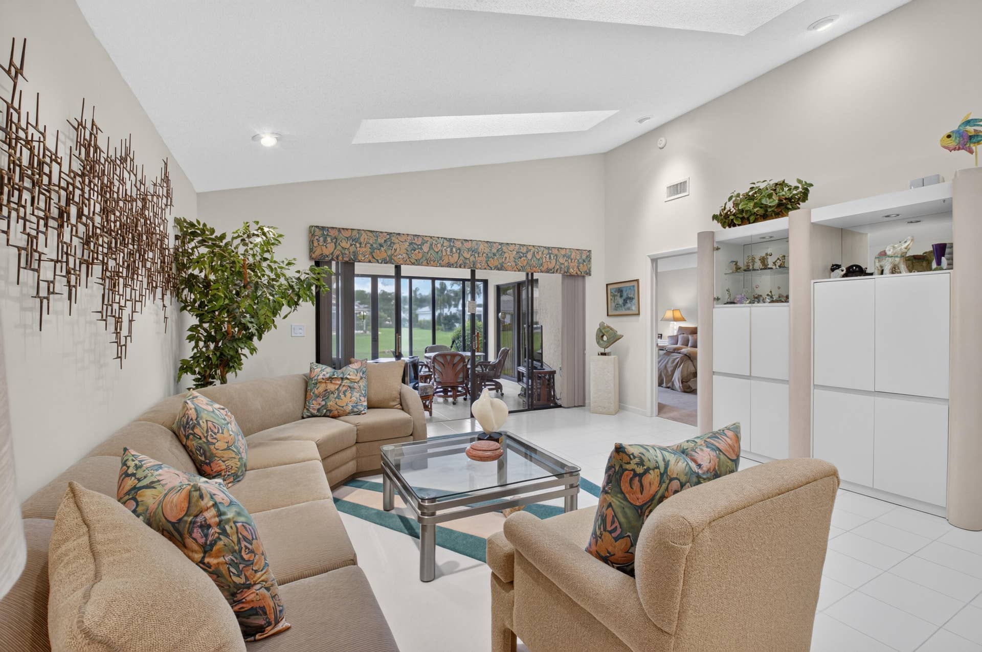 20065 Waters Edge Drive, #101, Boca Raton, FL 33434 Bright, open living area featuring a curved sectional sofa arrangement, glass-top coffee table, and abundant natural light from multi-panel glass doors